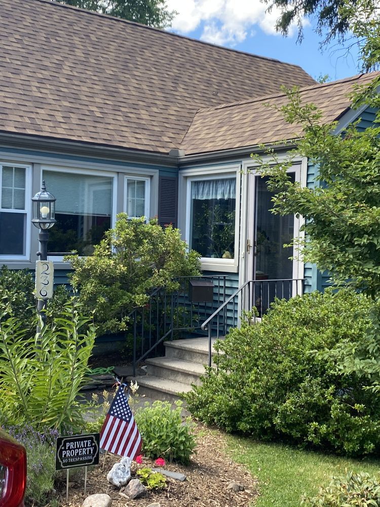 Blue house with brown roof, a small front porch, and US flag in the front yard.