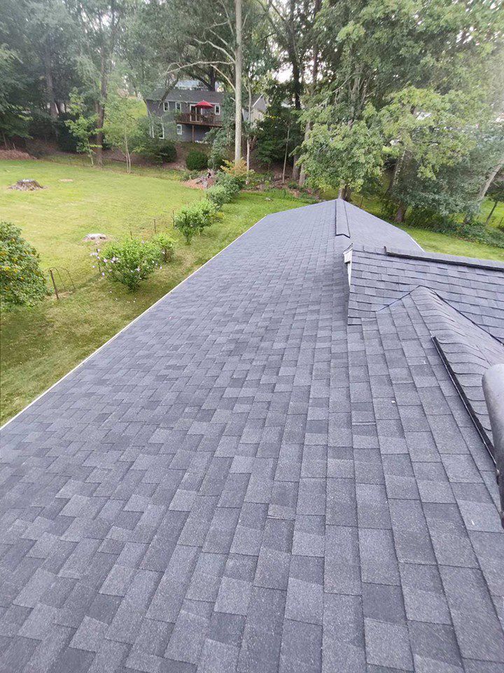 Dark gray shingle roof stretches toward a green yard with trees in the background.