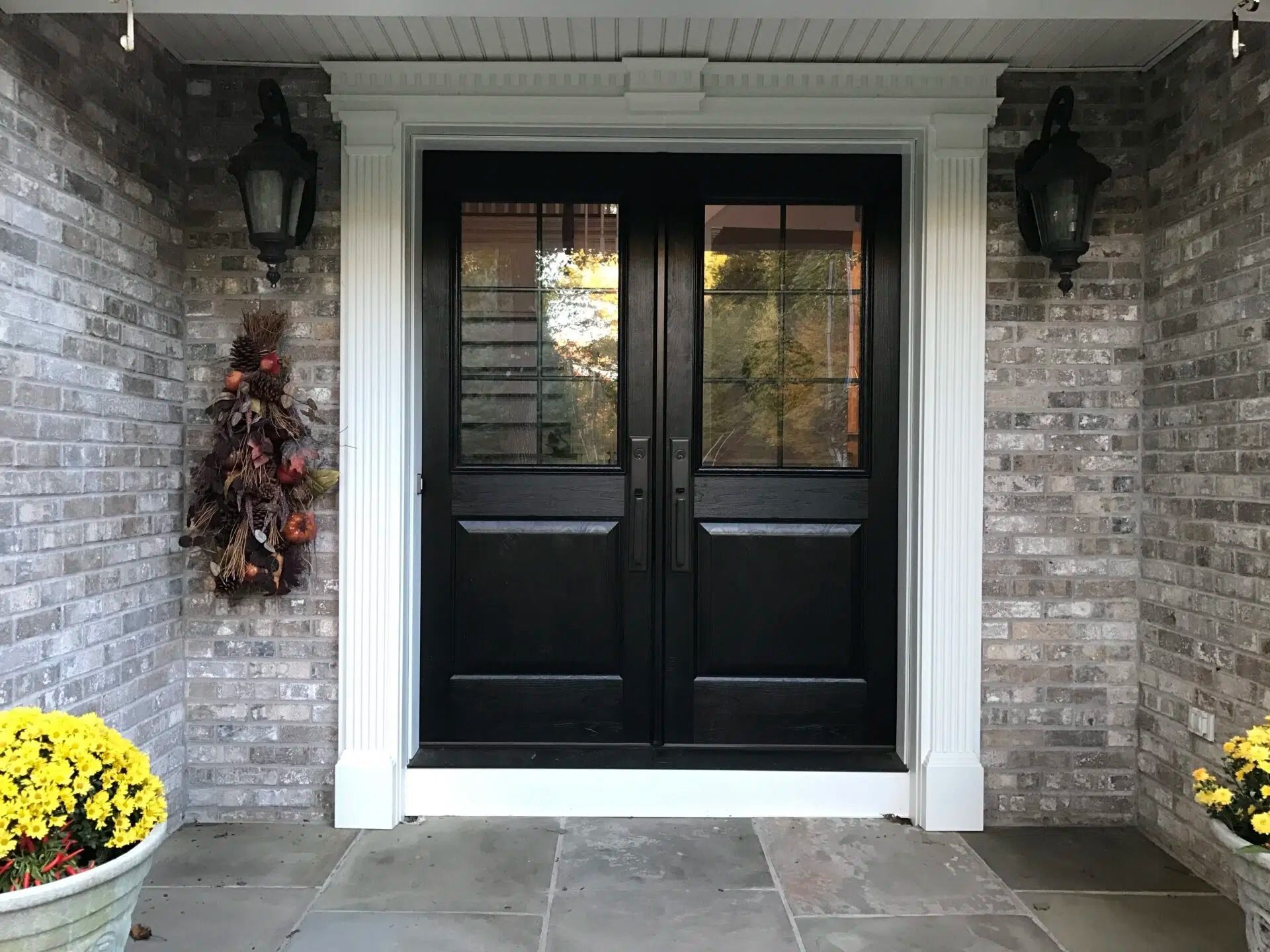 Black double front doors with glass panels, white trim, brick wall, and lanterns.