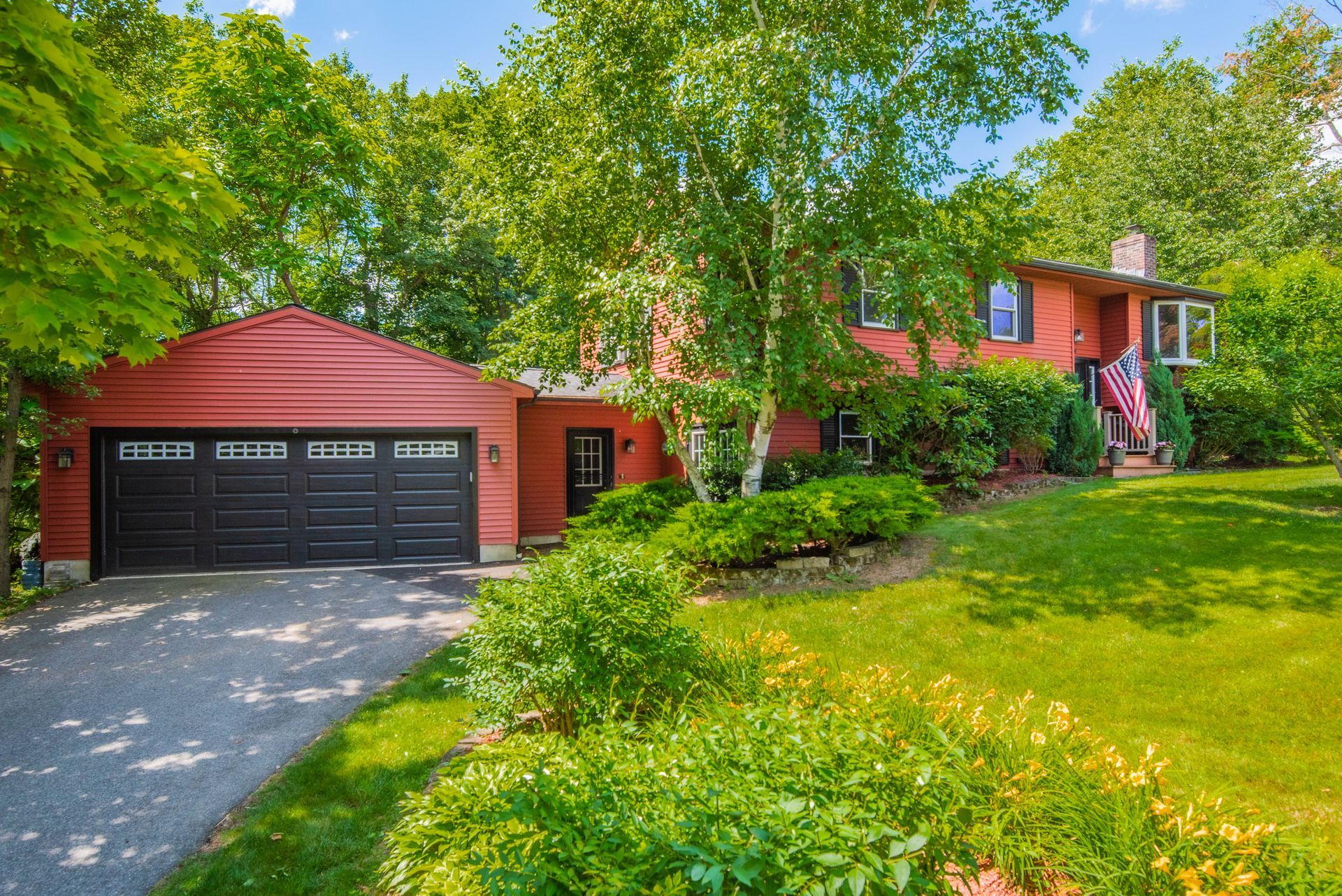 Red house with black garage door, surrounded by green trees and a grassy yard.