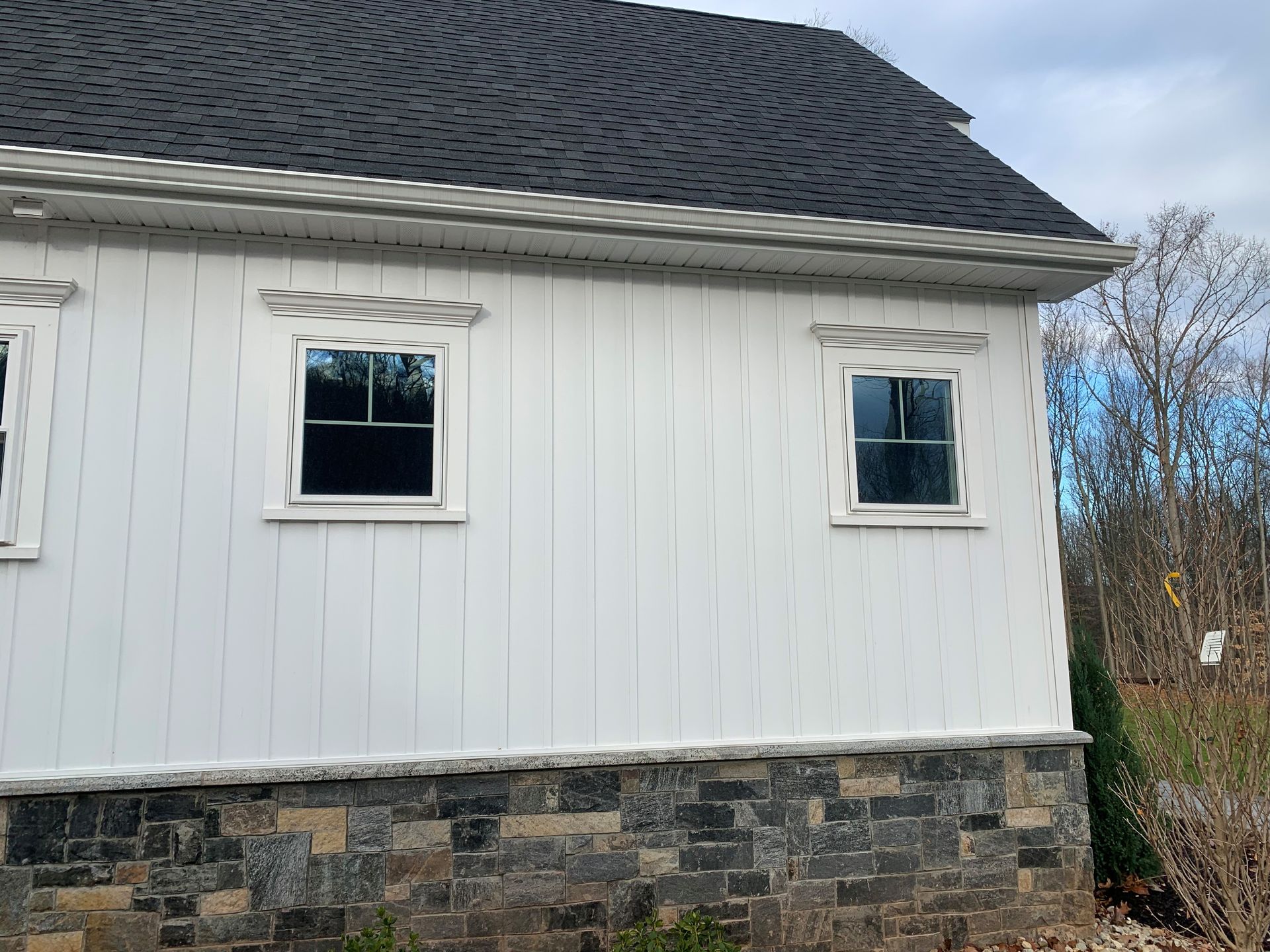 White building with dark roof, windows, and stone base against a cloudy sky.