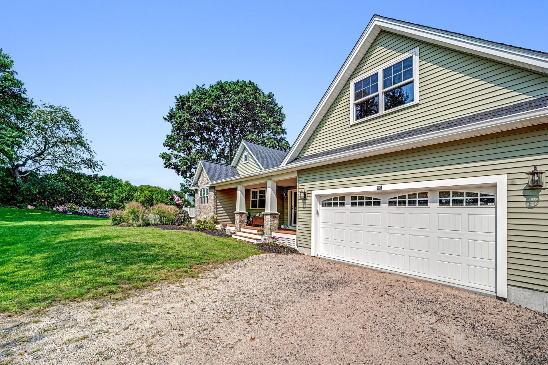 Green house with white garage door on gravel driveway, blue sky.
