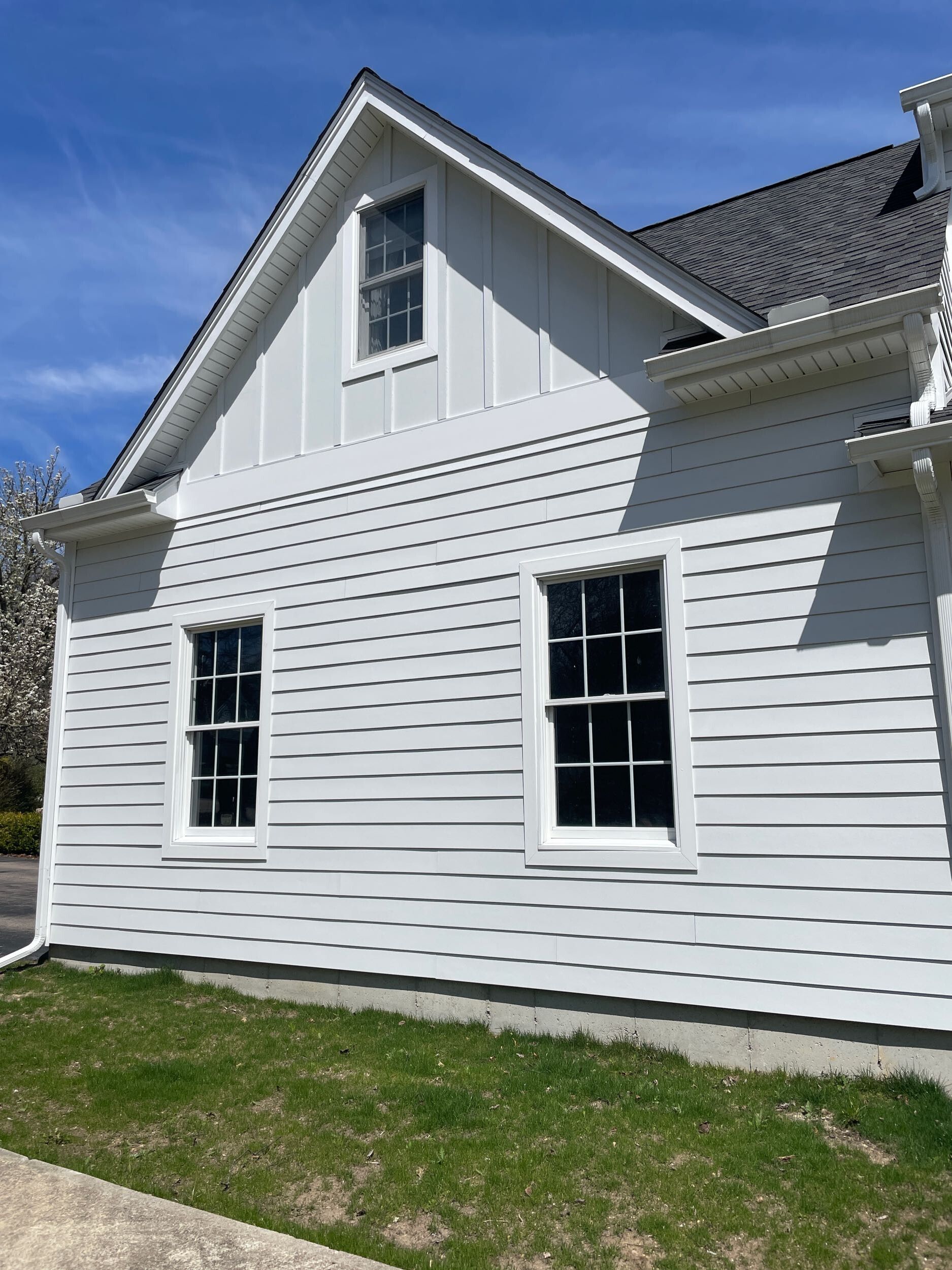 White house with black roof, two windows, and a small patch of green grass.