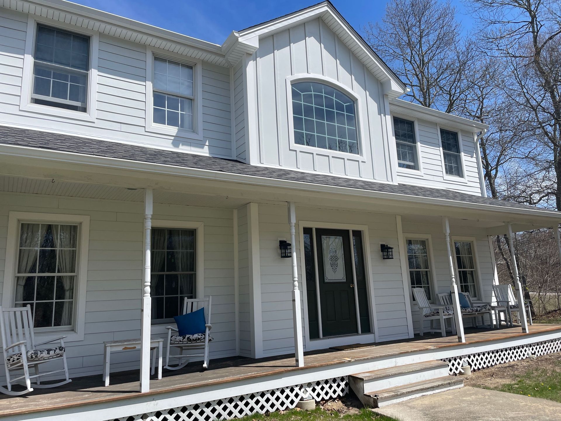 White two-story house with a large front porch. Rocking chairs sit on the porch.