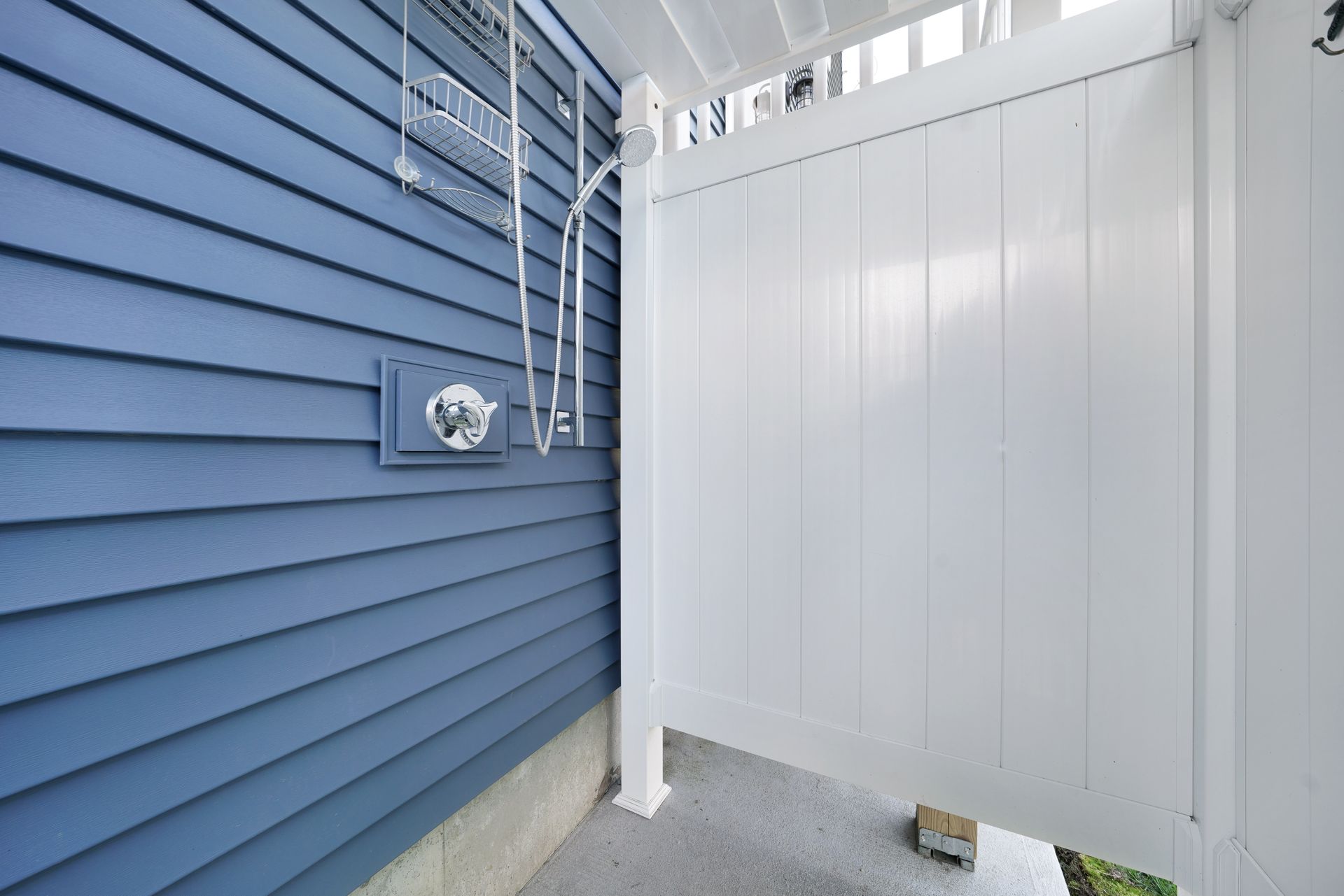 Blue siding next to a white outdoor shower with chrome fixtures.