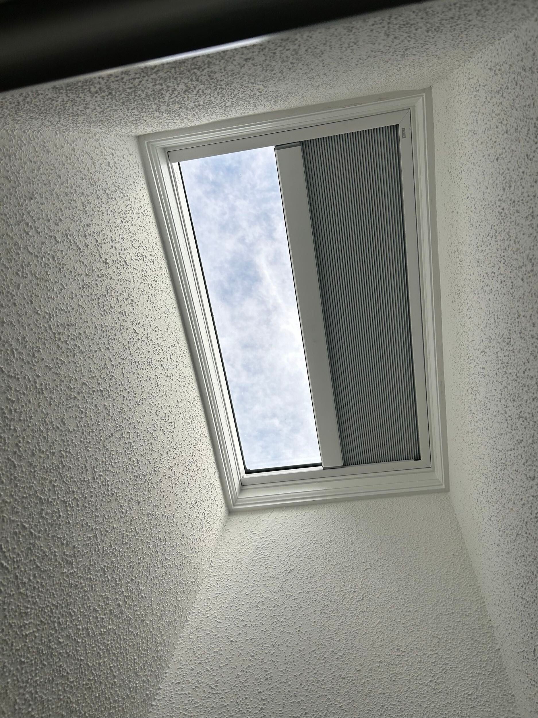 Skylight in a textured white wall, showing a view of the sky and a building.