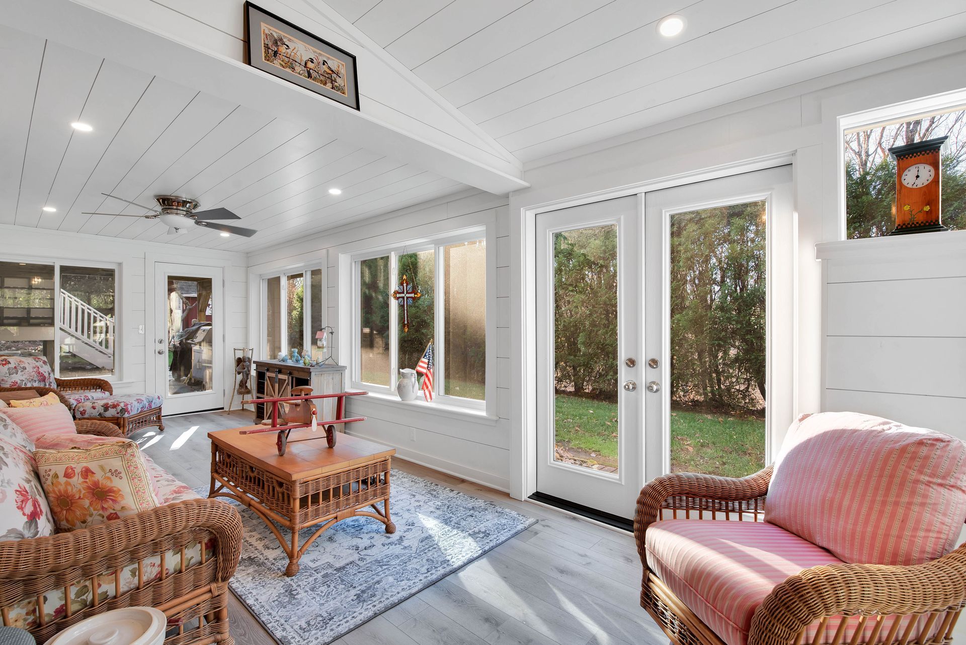 Sunroom with wicker furniture, French doors to yard, white paneled walls and ceiling.