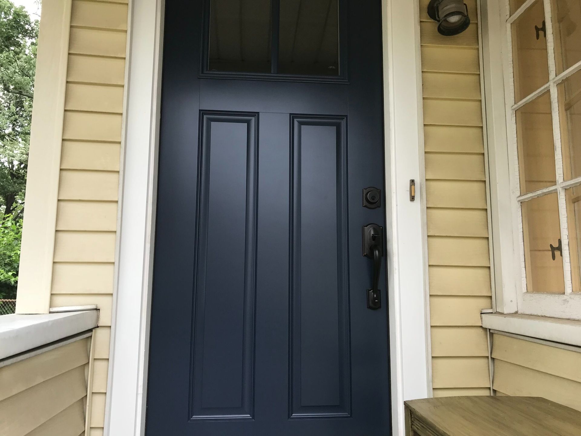 Blue front door with sidelight, surrounded by yellow siding and white trim.