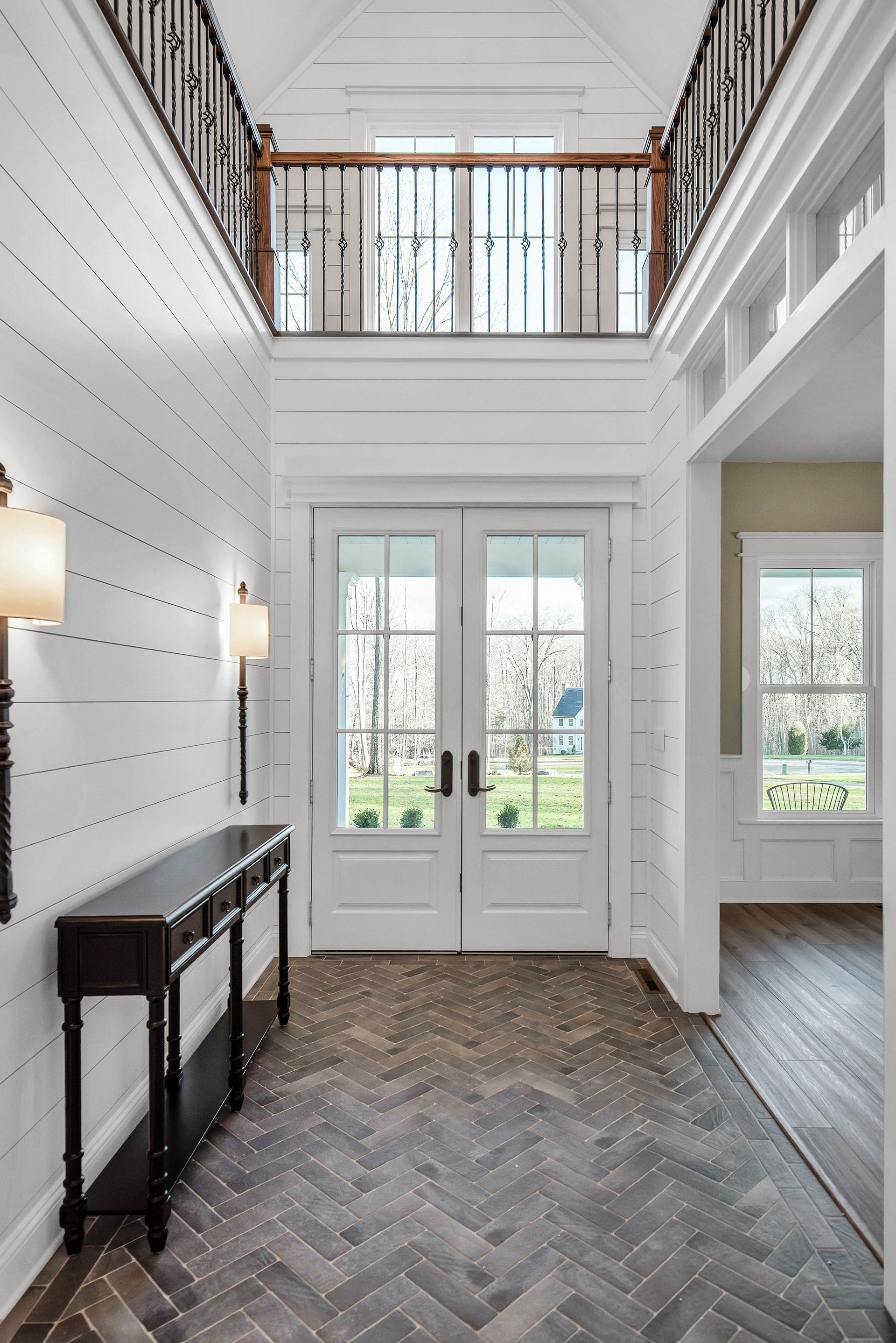 Entryway with white paneling, double doors, dark wood console table, and a herringbone floor.