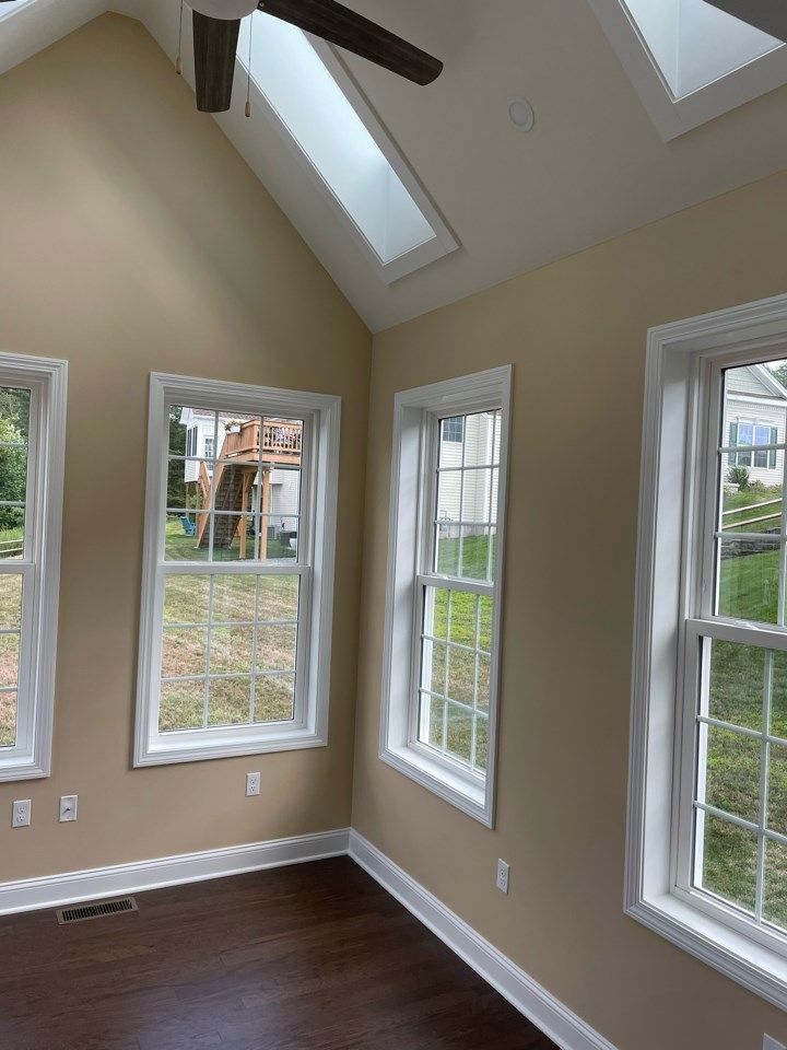 Interior room with windows, skylights, and a ceiling fan; tan walls, white trim, and dark wood floor.