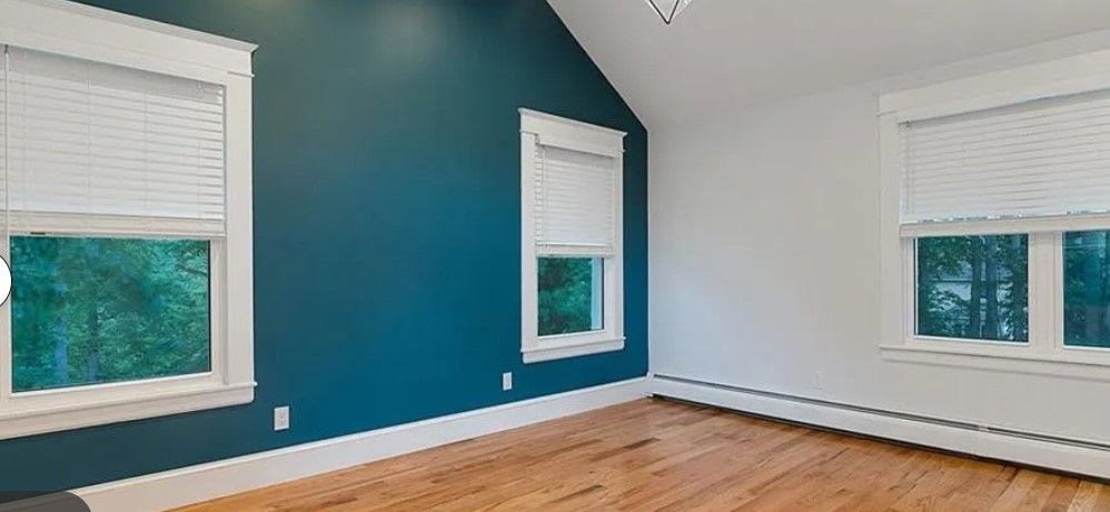 An empty room with wood floors and windows. The walls are teal and white.