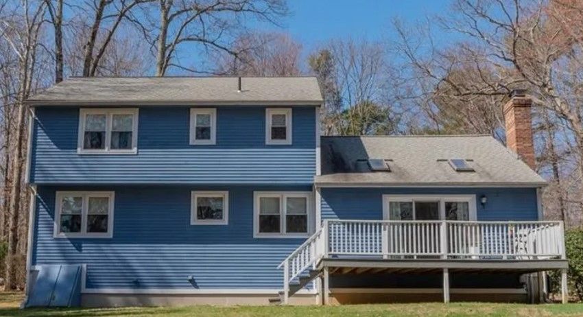 Blue two-story house with white trim, deck, and a brick chimney under a blue sky.