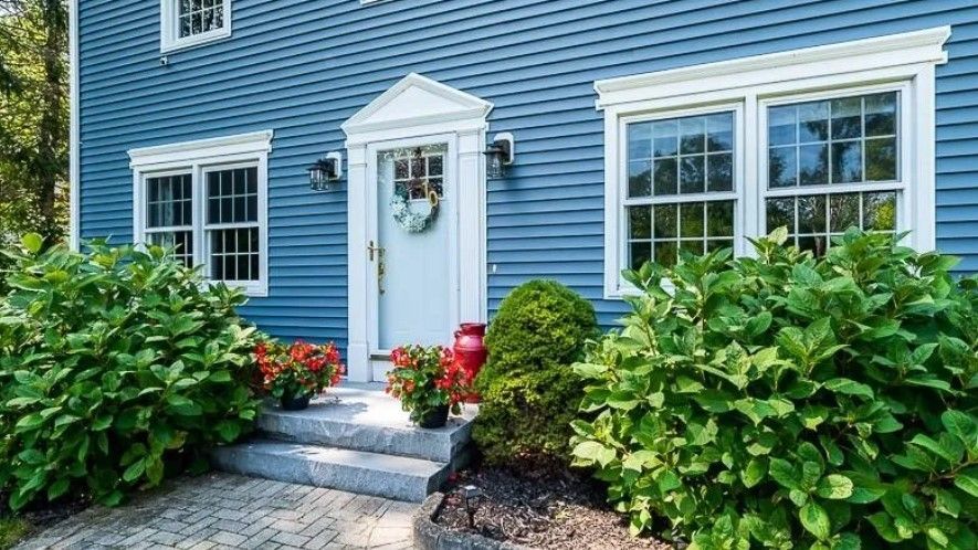 Blue house with white trim, steps, and bushes with red flowers.