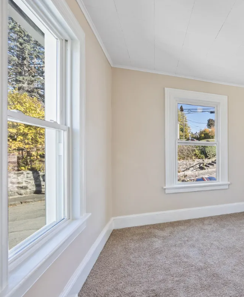 Interior of a room with two white-framed windows, beige walls, and carpet.