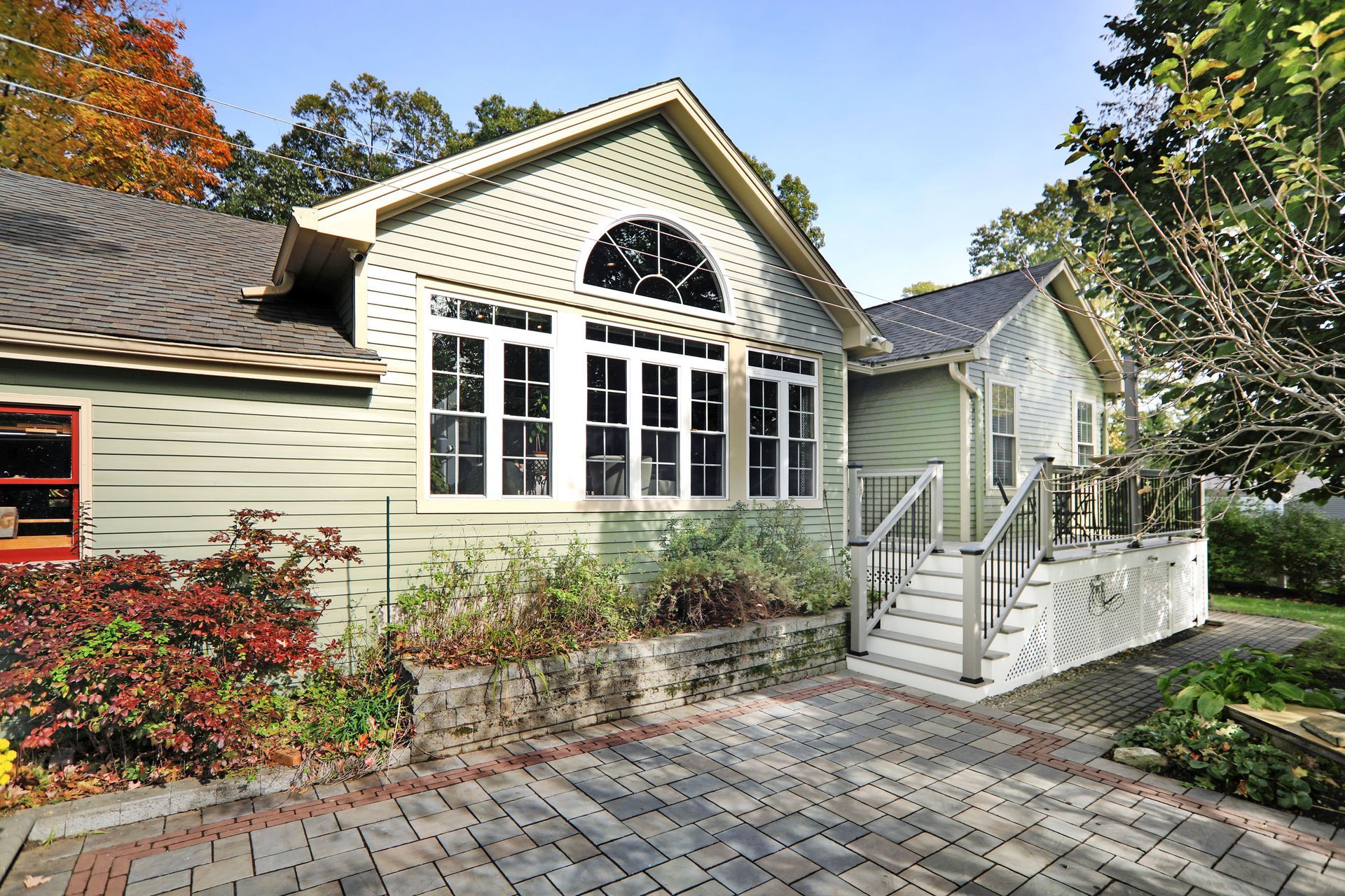 Light green house with white trim, arched window, and gray roof. Brick patio and steps.