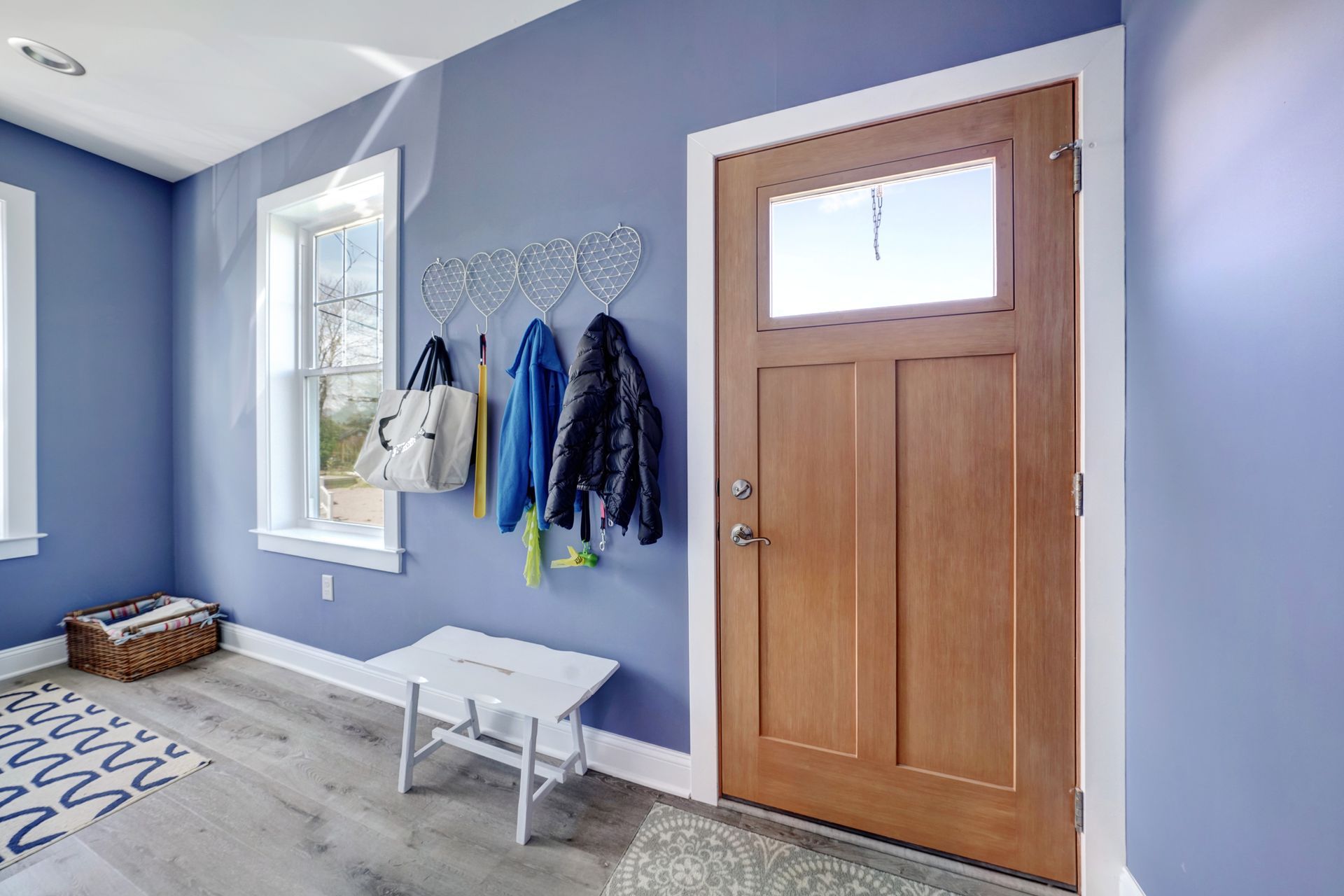 Blue entryway with wooden door, window, coat rack, bench, and light wood-look flooring.