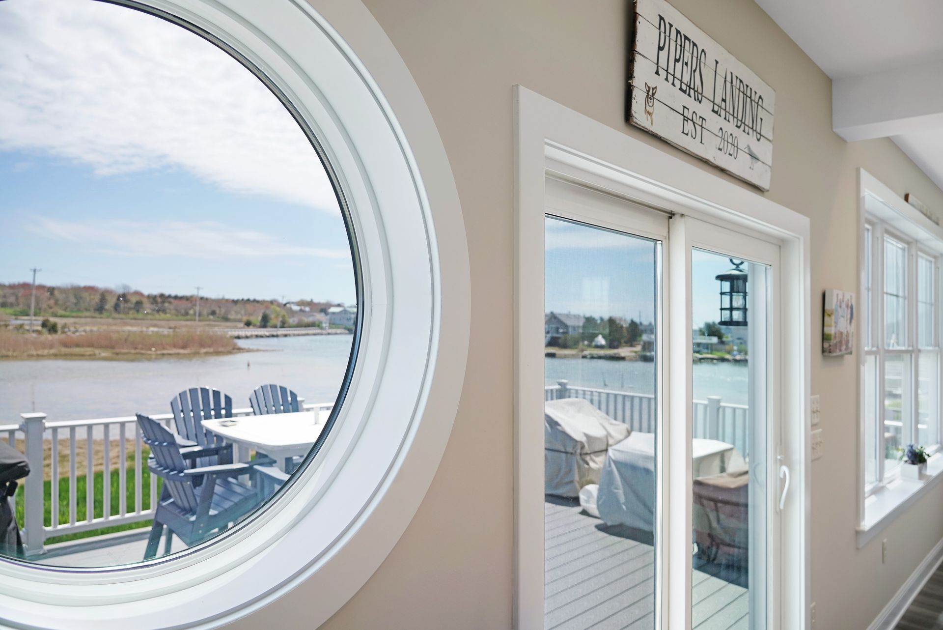 Interior view with round window and sliding glass door, both overlooking a deck with water view.