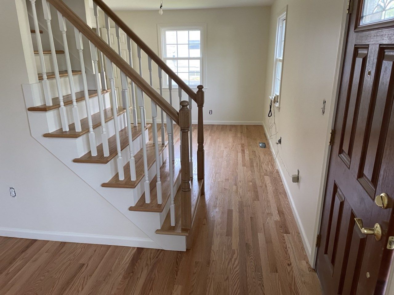 Interior view: staircase with wooden steps and railing, hardwood floors, and a front door.