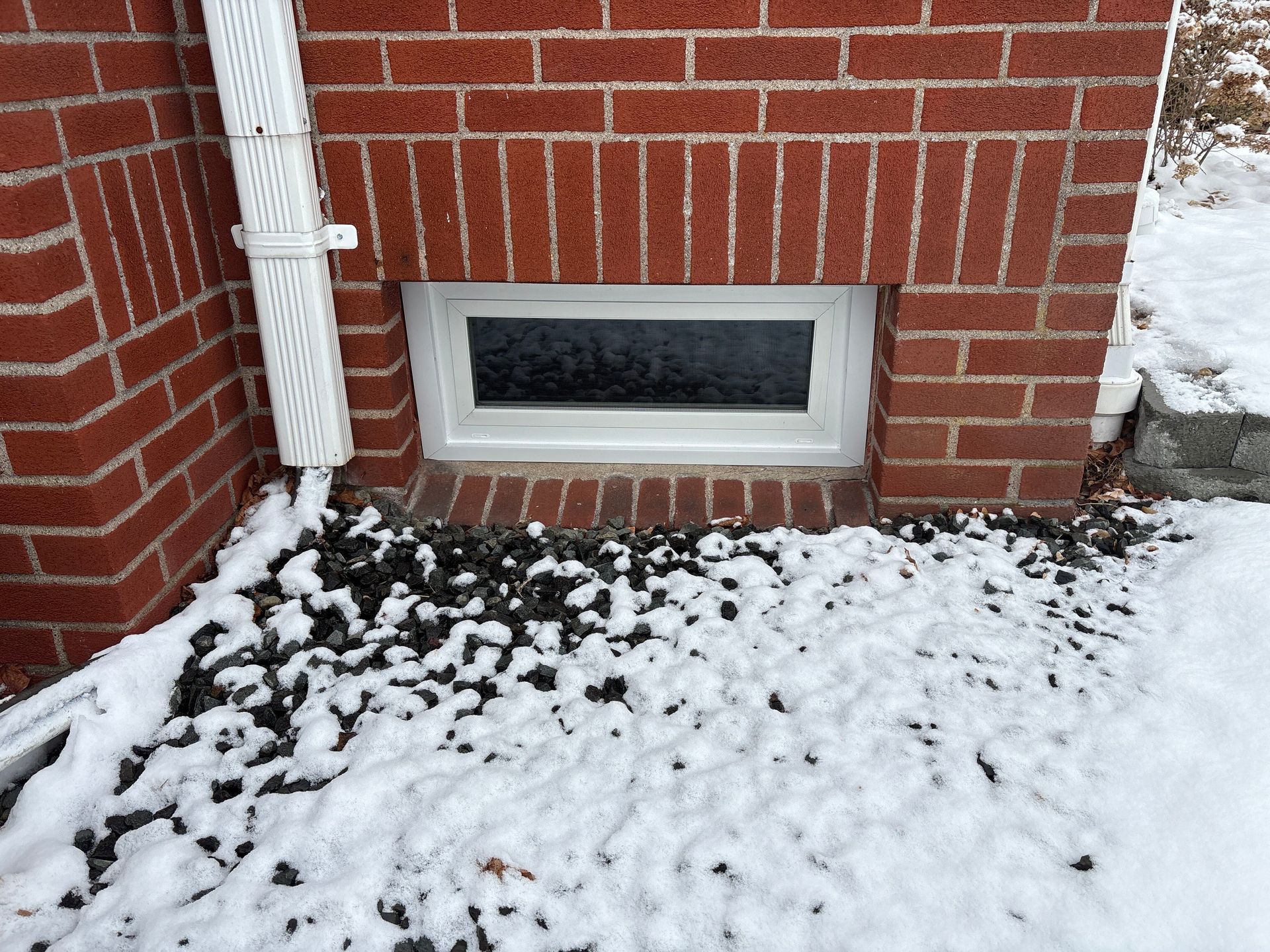 Brick building with a window and white trim, snow-covered ground, and black rocks.