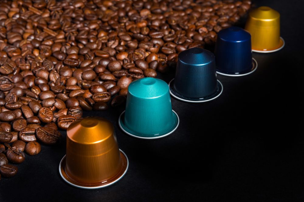 Chicchi di caffè e cinque cialde di caffè colorate su una superficie nera.