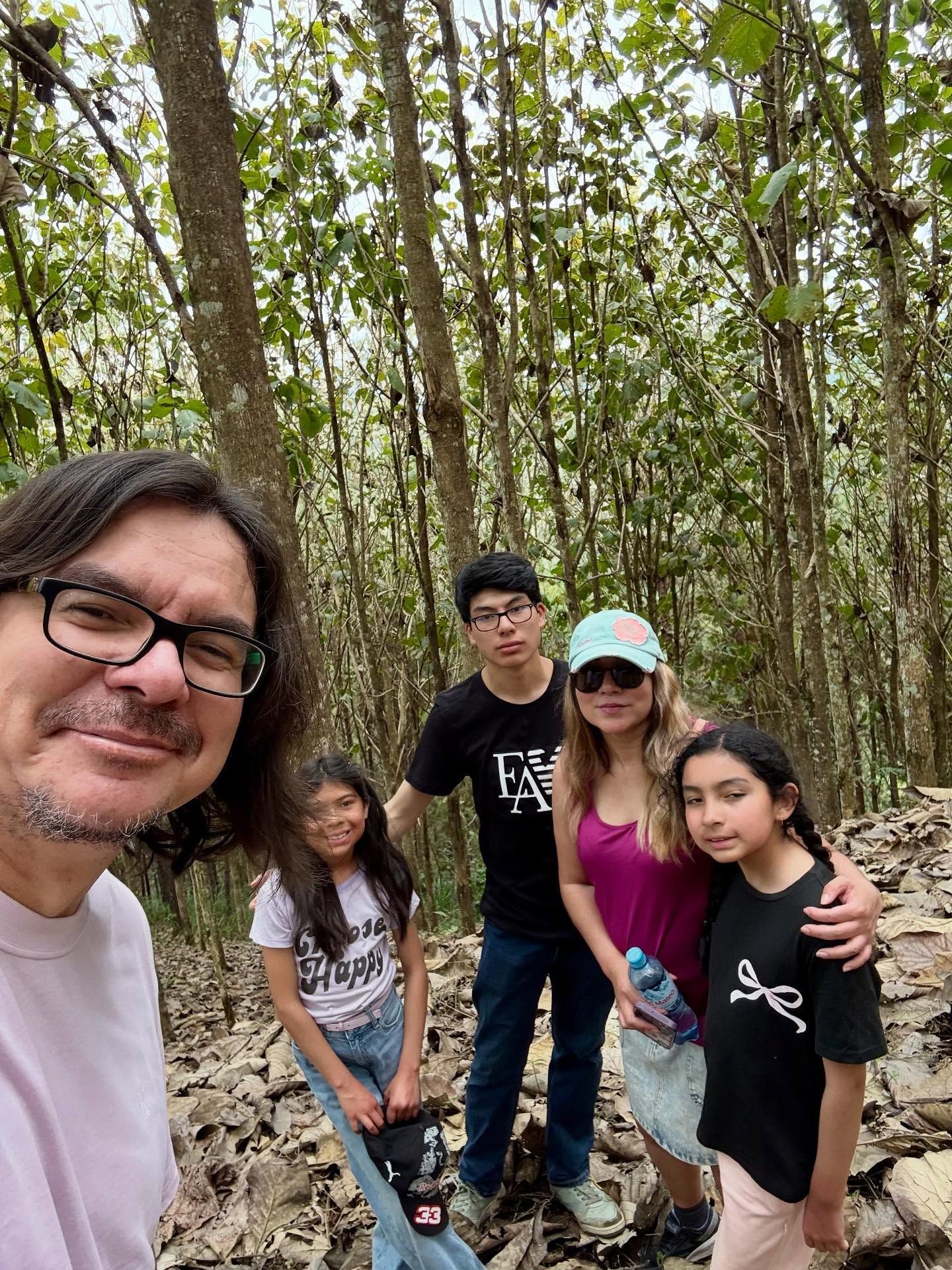 Una familia de cinco en un bosque, posando para una selfi. Rodeados de árboles.