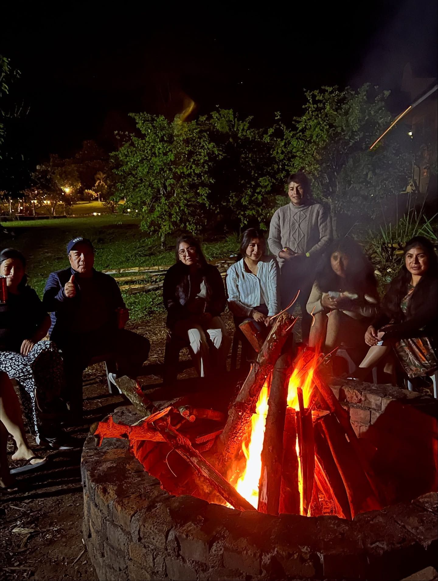 La gente se sienta alrededor de una fogata por la noche. Las llamas brillantes iluminan los rostros. .