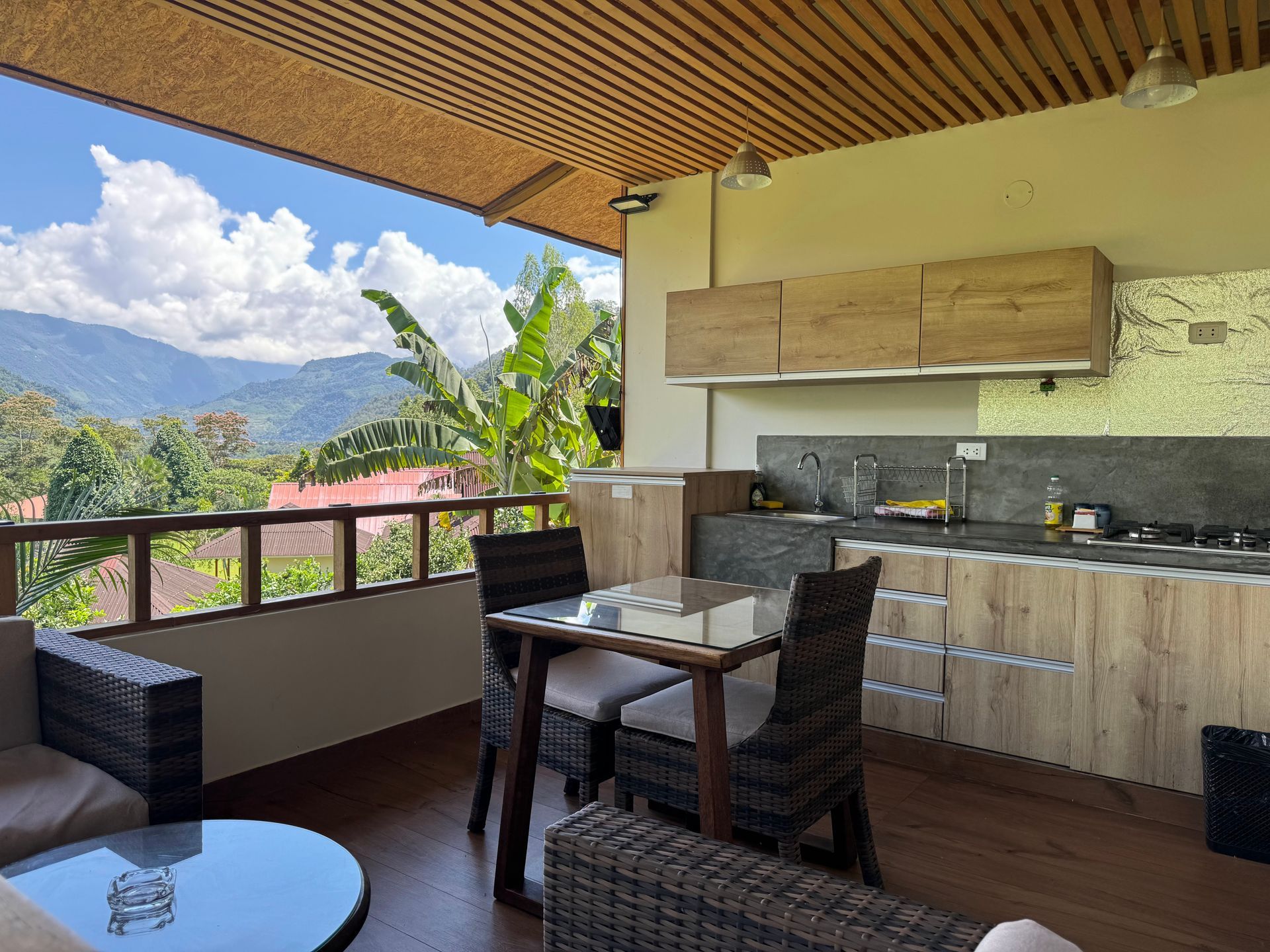 Cocina al aire libre con gabinetes de madera, mesa y sillas con vista a la montaña.