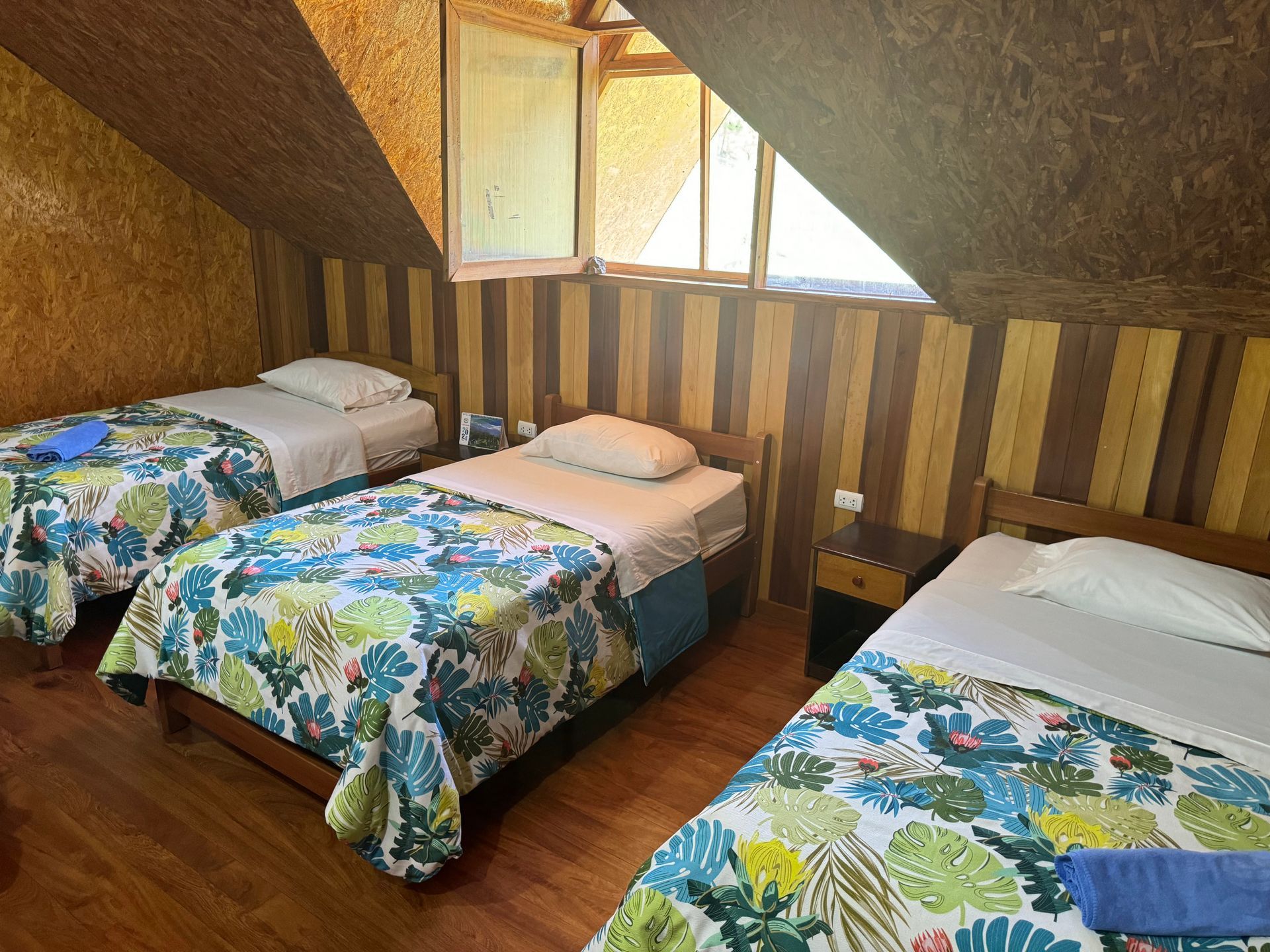 Un dormitorio con tres camas individuales con edredones de estampado tropical, paredes de madera.
