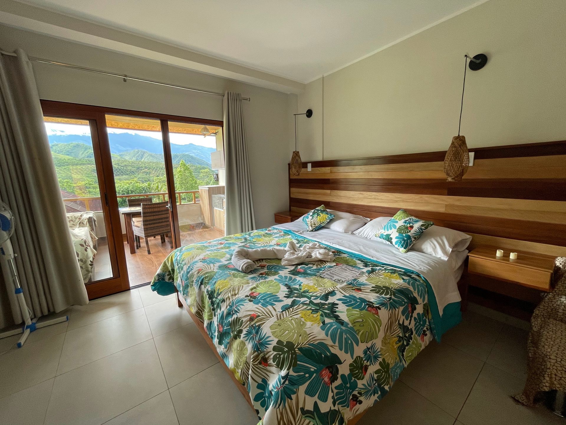 Una habitación de hotel con una cama con un edredón de estampado de hojas de colores, un cabecero de listones de madera.
