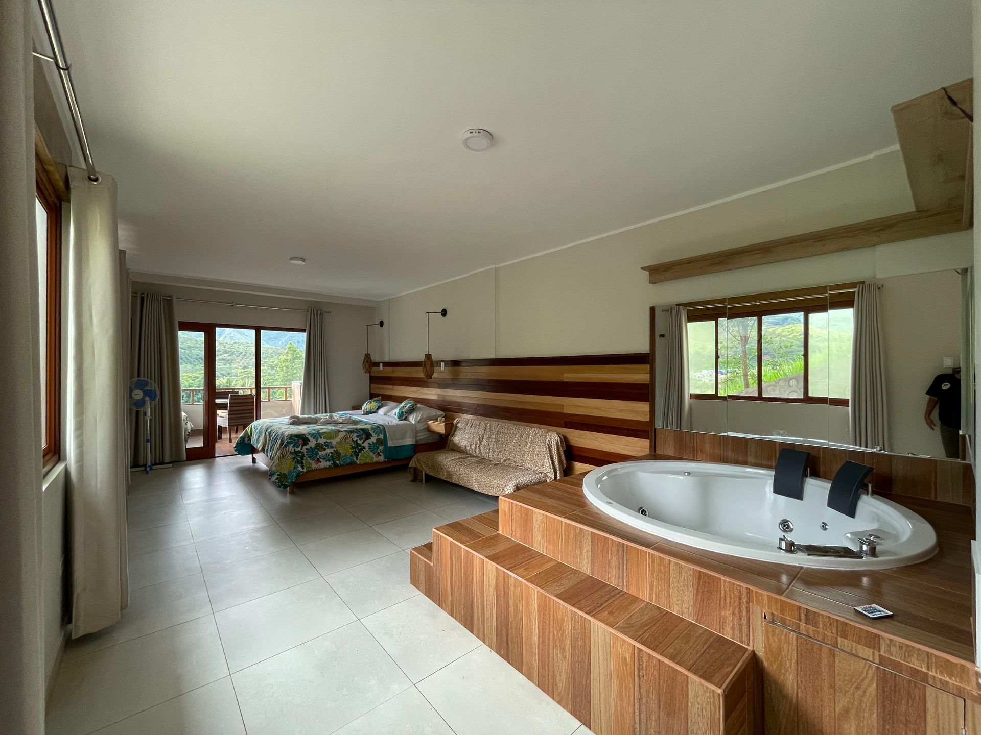 Amplia habitación de hotel con bañera de hidromasaje en primer plano, una cama con ropa de cama colorida.