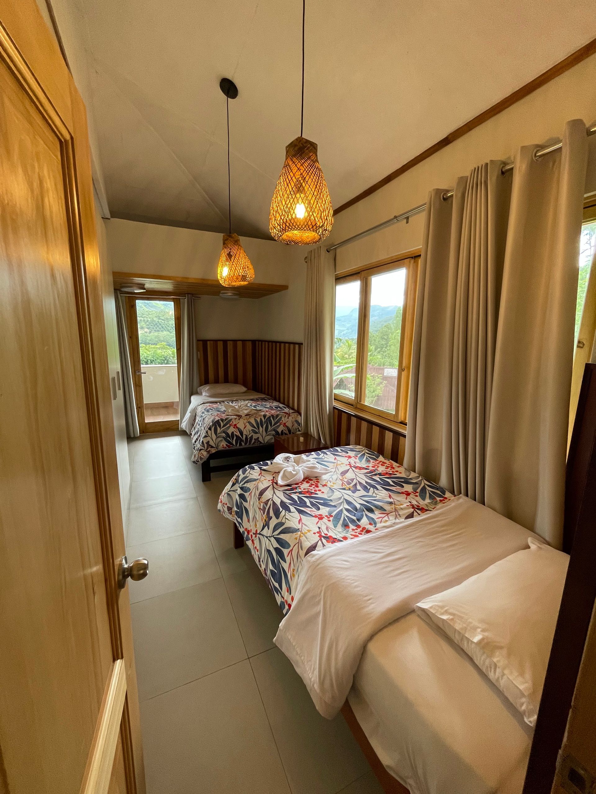 Dormitorio con dos camas individuales, ropa de cama floral, cabeceros de madera, lámparas colgantes y vistas.