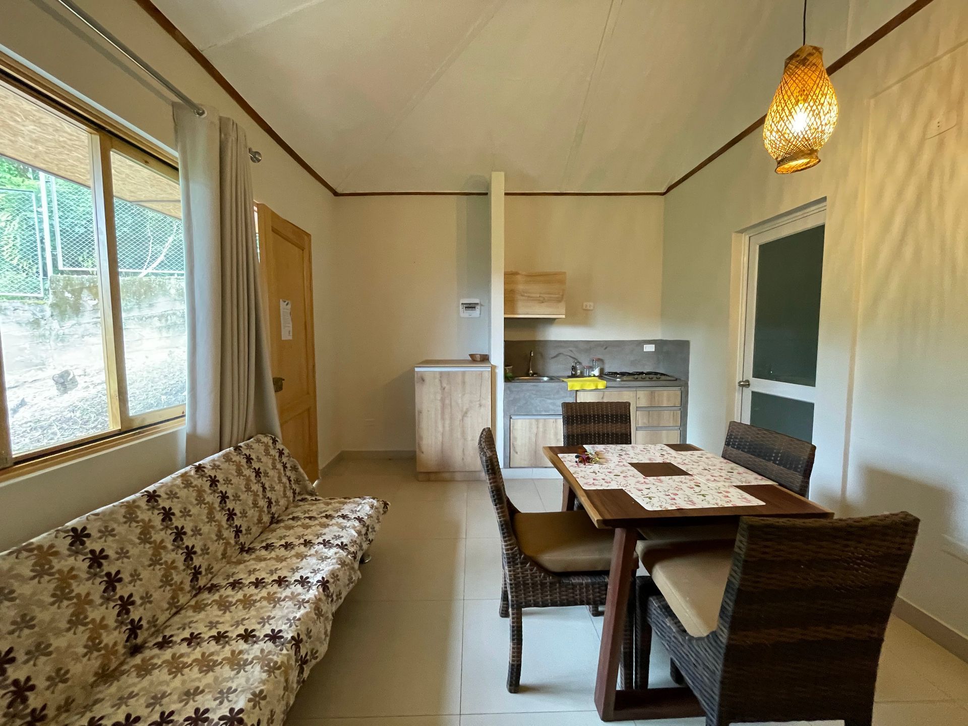 Interior de una pequeña habitación con sofá, mesa de comedor y cocina americana. Paredes beige, detalles en madera.