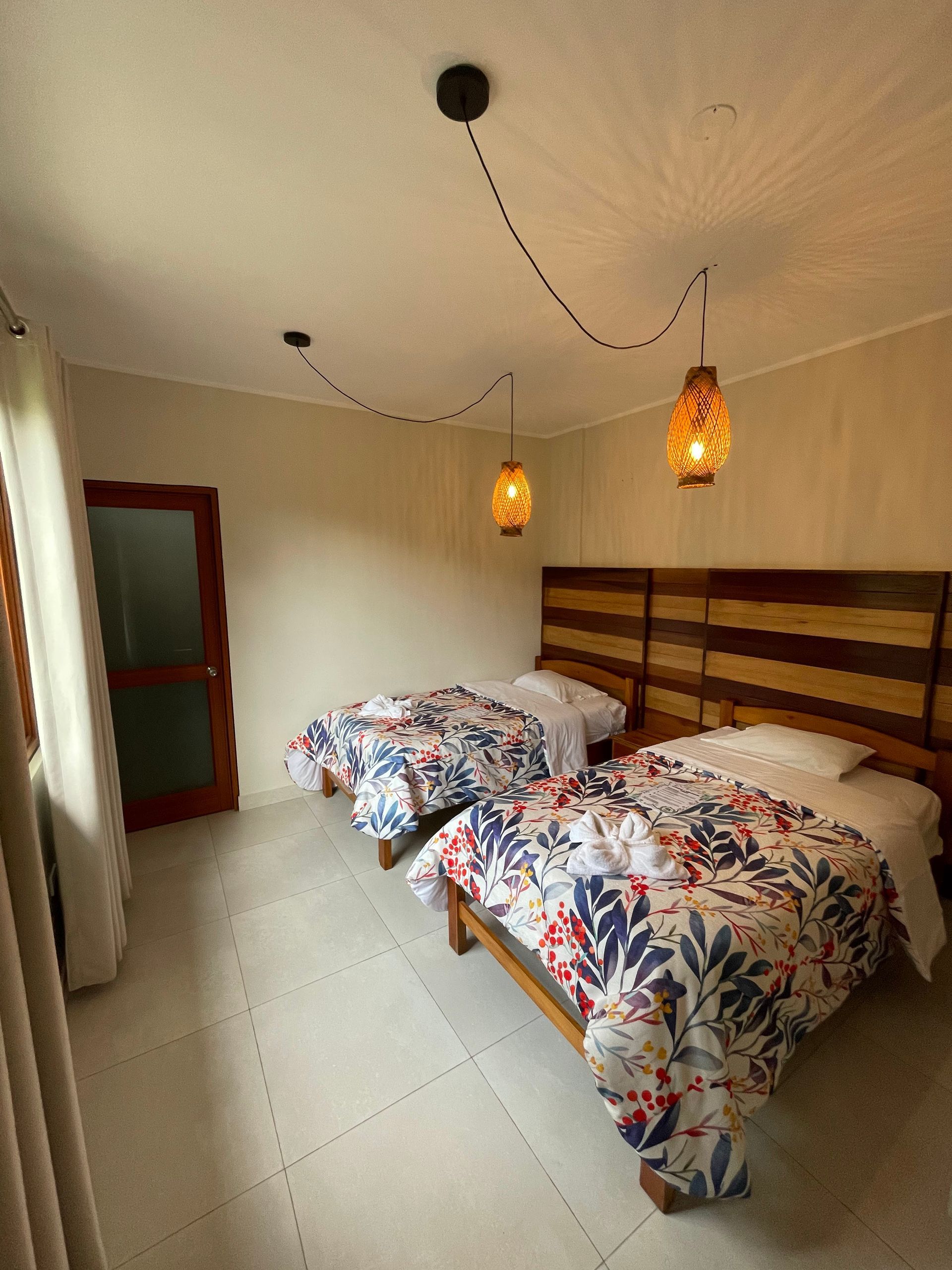 Una habitación de hotel con dos camas individuales con colchas estampadas, cabeceros de madera y lámparas colgantes.