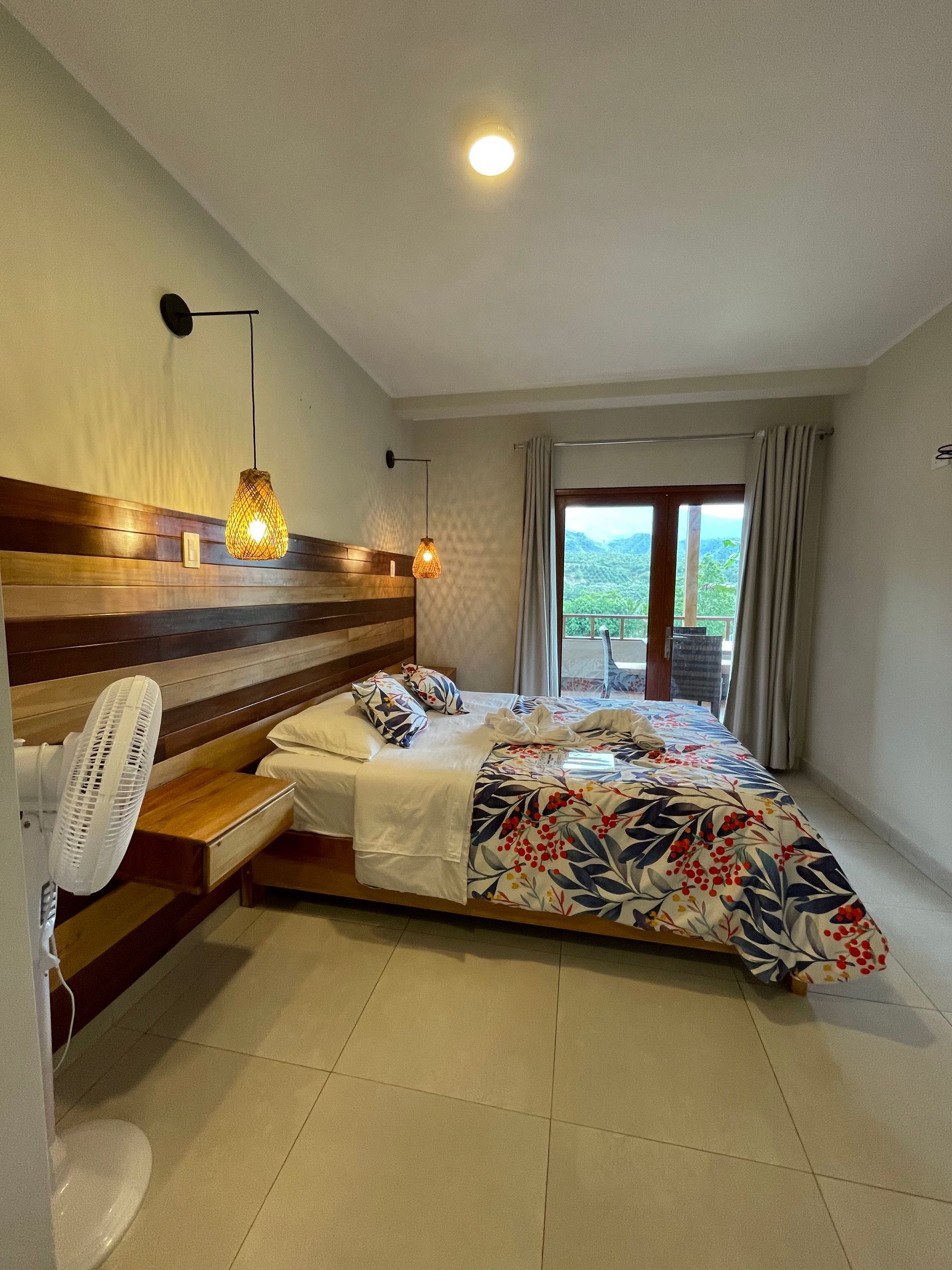 Un dormitorio moderno con cabecero de madera, lámparas colgantes y una colcha con estampado floral cerca de una puerta.