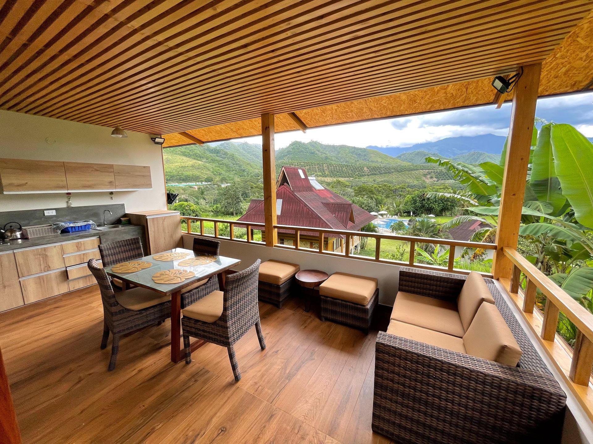Un patio al aire libre con un juego de comedor y un sofá de mimbre, con vistas a un frondoso valle de montaña.