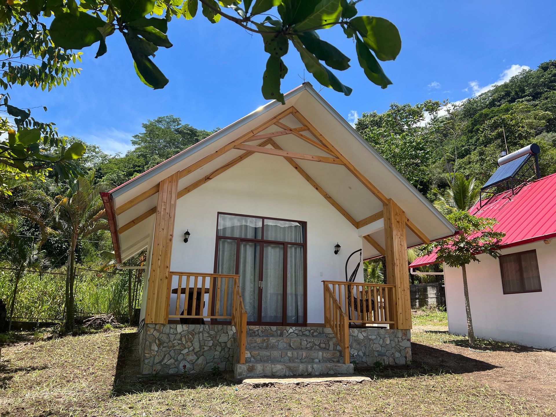 Una cabaña de vacaciones blanca con pilares de madera y base de piedra, situada en un entorno exterior exuberante, verde