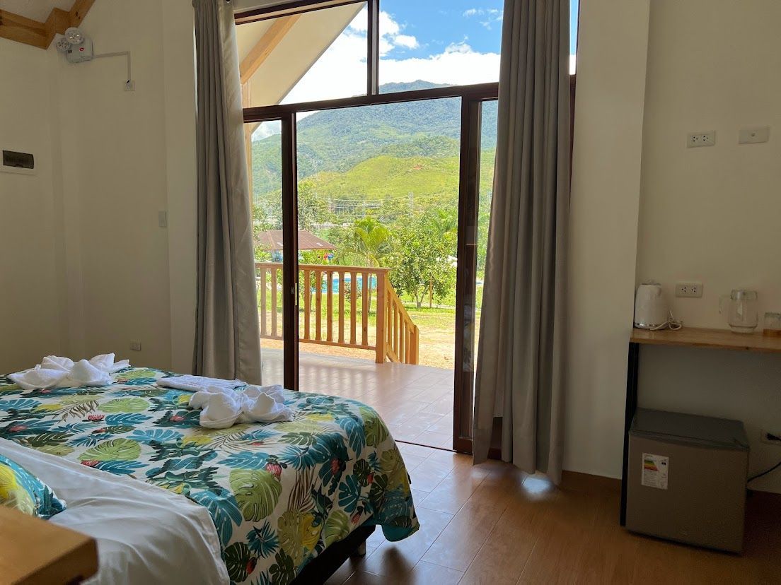 Una habitación de hotel con una cama con una colcha de estampado tropical y acceso a un balcón con vistas  a la montaña.