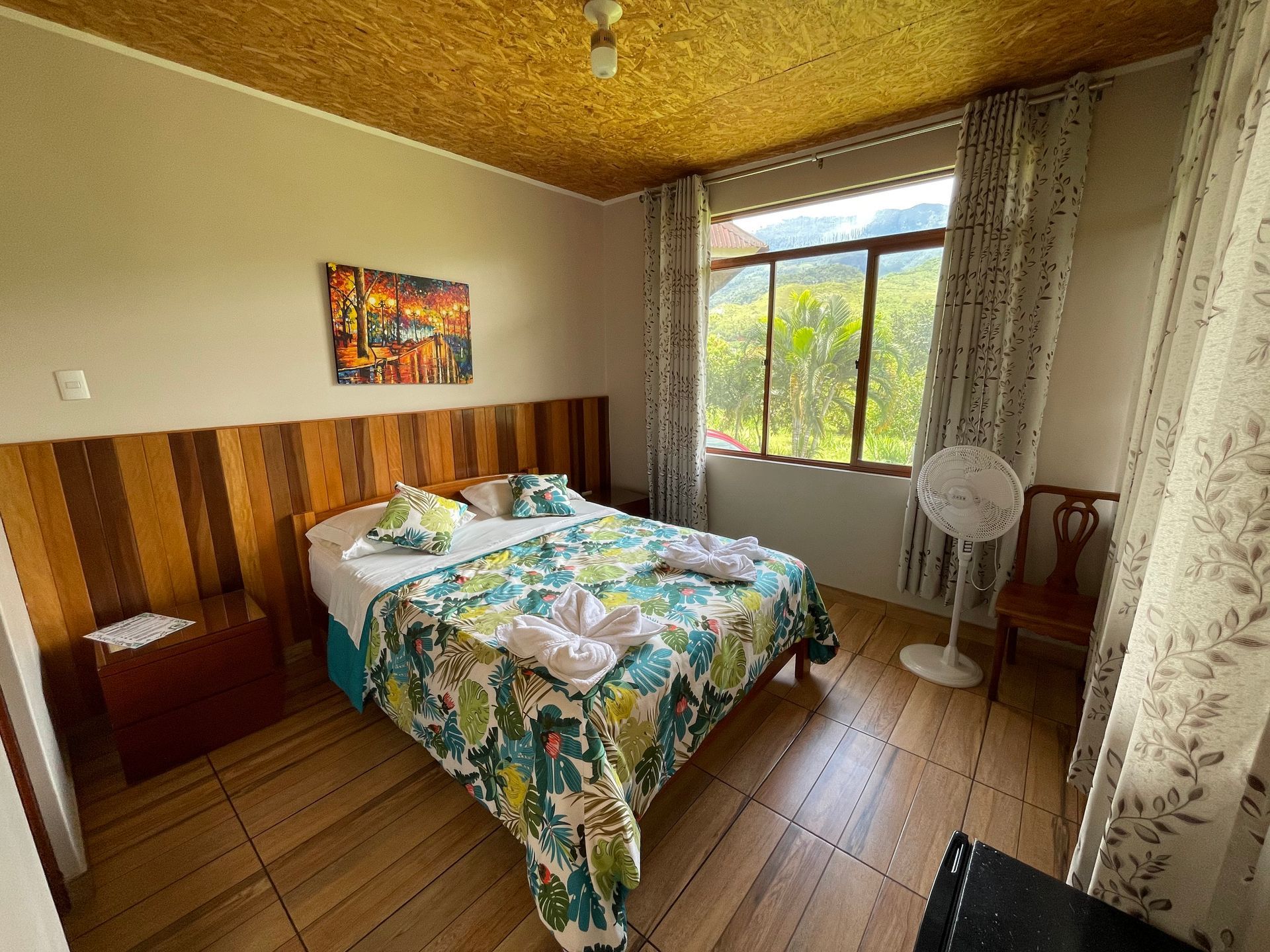 Un dormitorio con una cama doble con estampado floral, revestimiento de madera, una ventana grande.