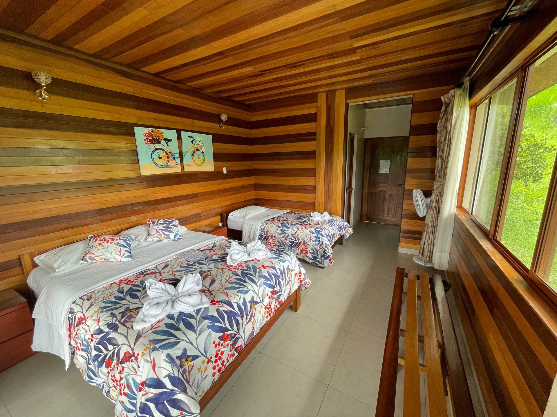 Una acogedora habitación de hotel con paneles de madera, dos camas con ropa de cama estampada con flores, abundante luz .