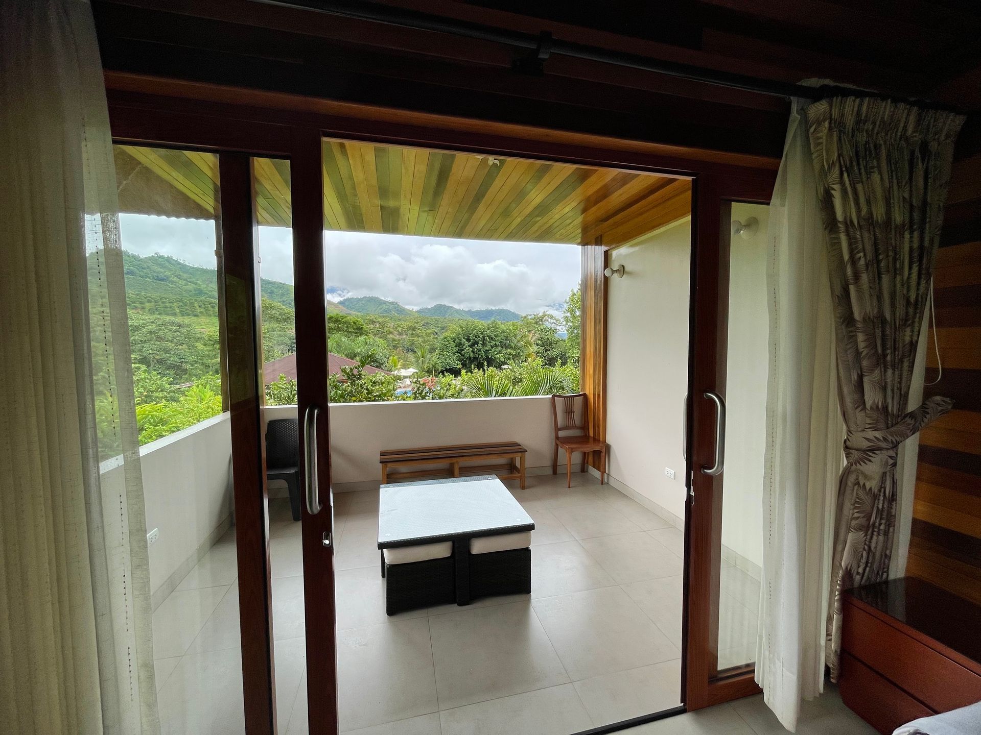 Un balcón con suelo de baldosas blancas, una mesa baja blanca y dos sillas, con vistas a un paisaje montañoso.