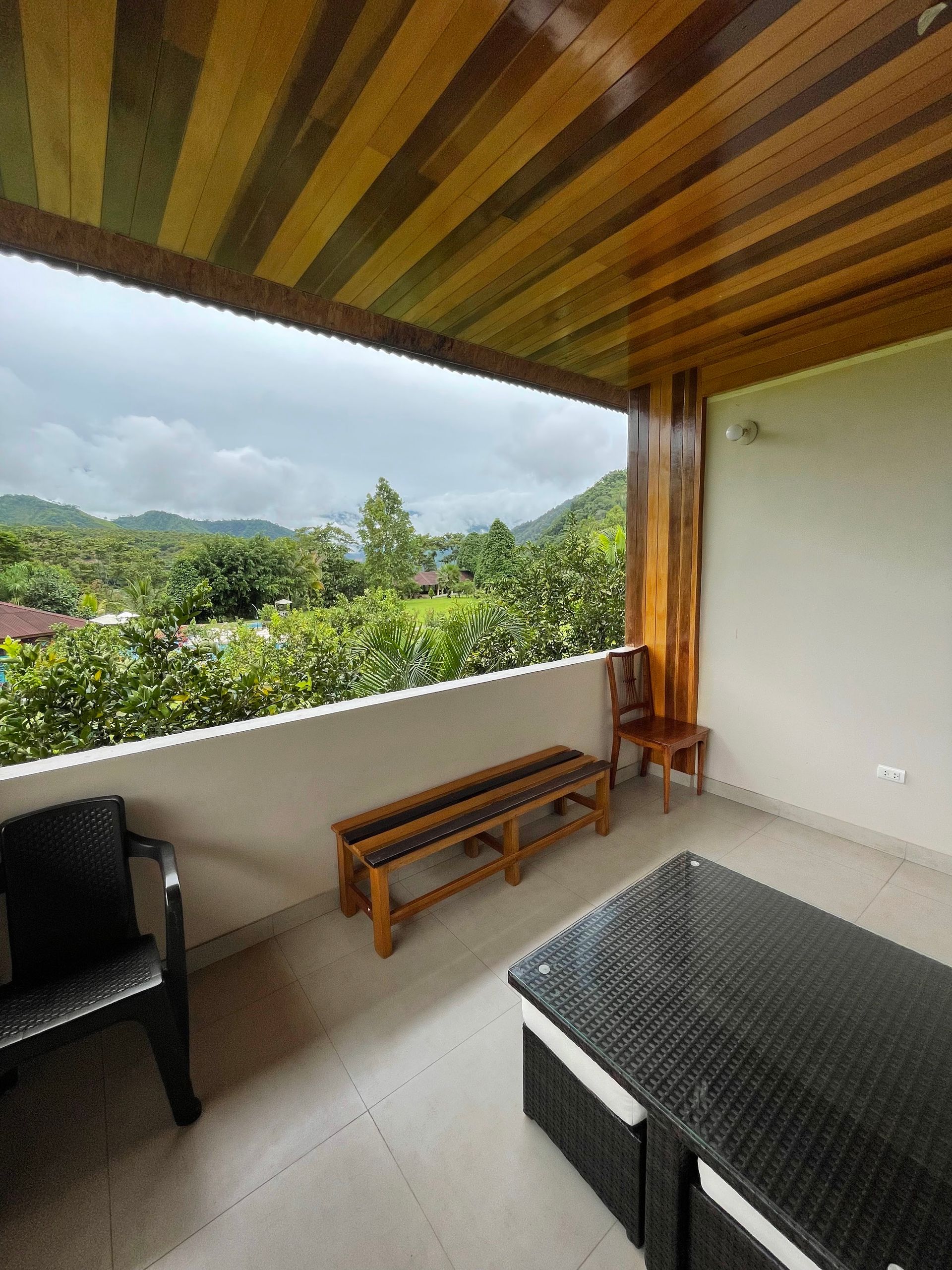 Un balcón cubierto con paneles de madera en el techo, con vistas a un paisaje verde y frondoso de colinas.