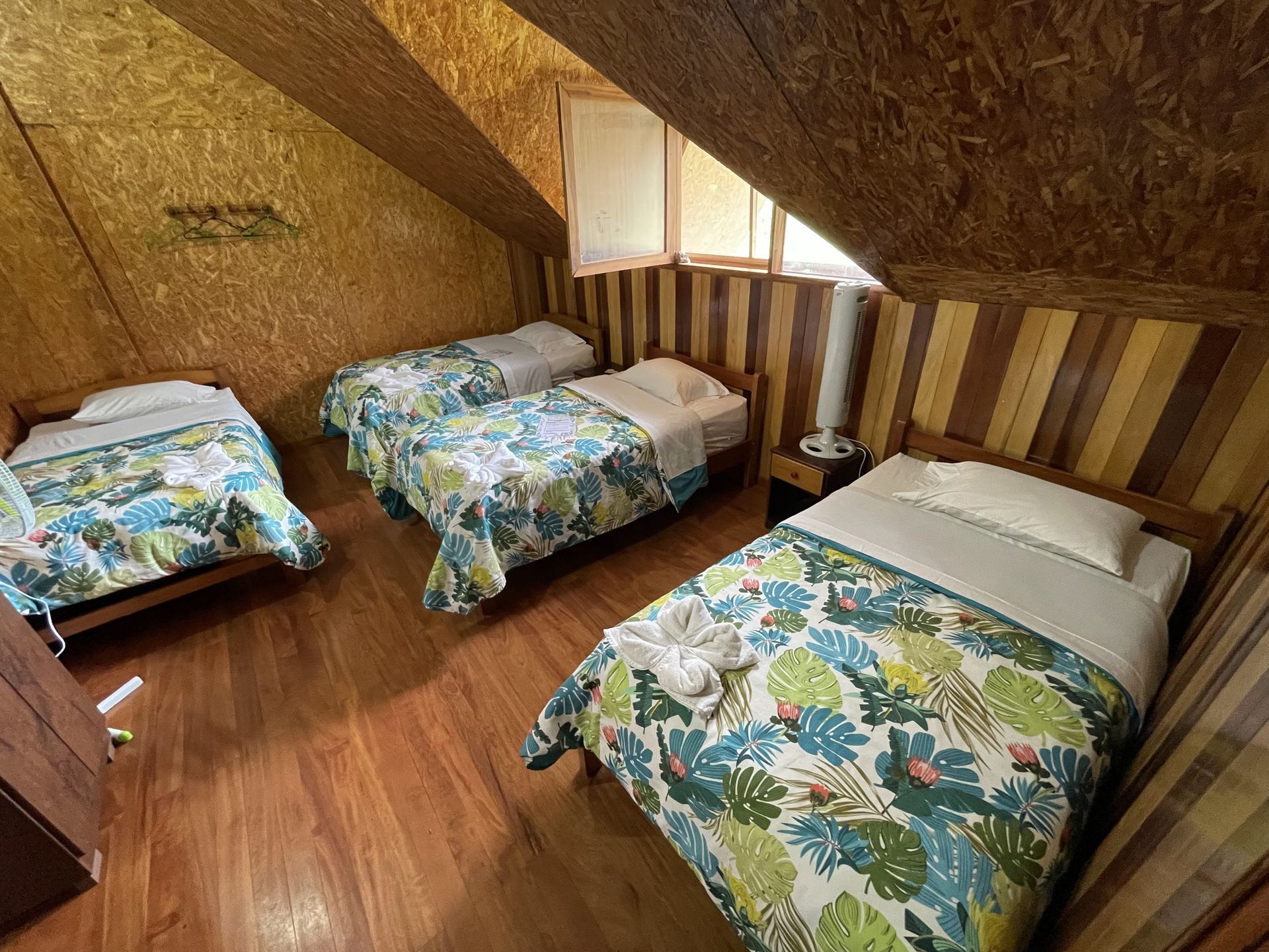 Un dormitorio abuhardillado con paredes y suelo revestidos de madera cuenta con tres camas individuales con ropa de cama.