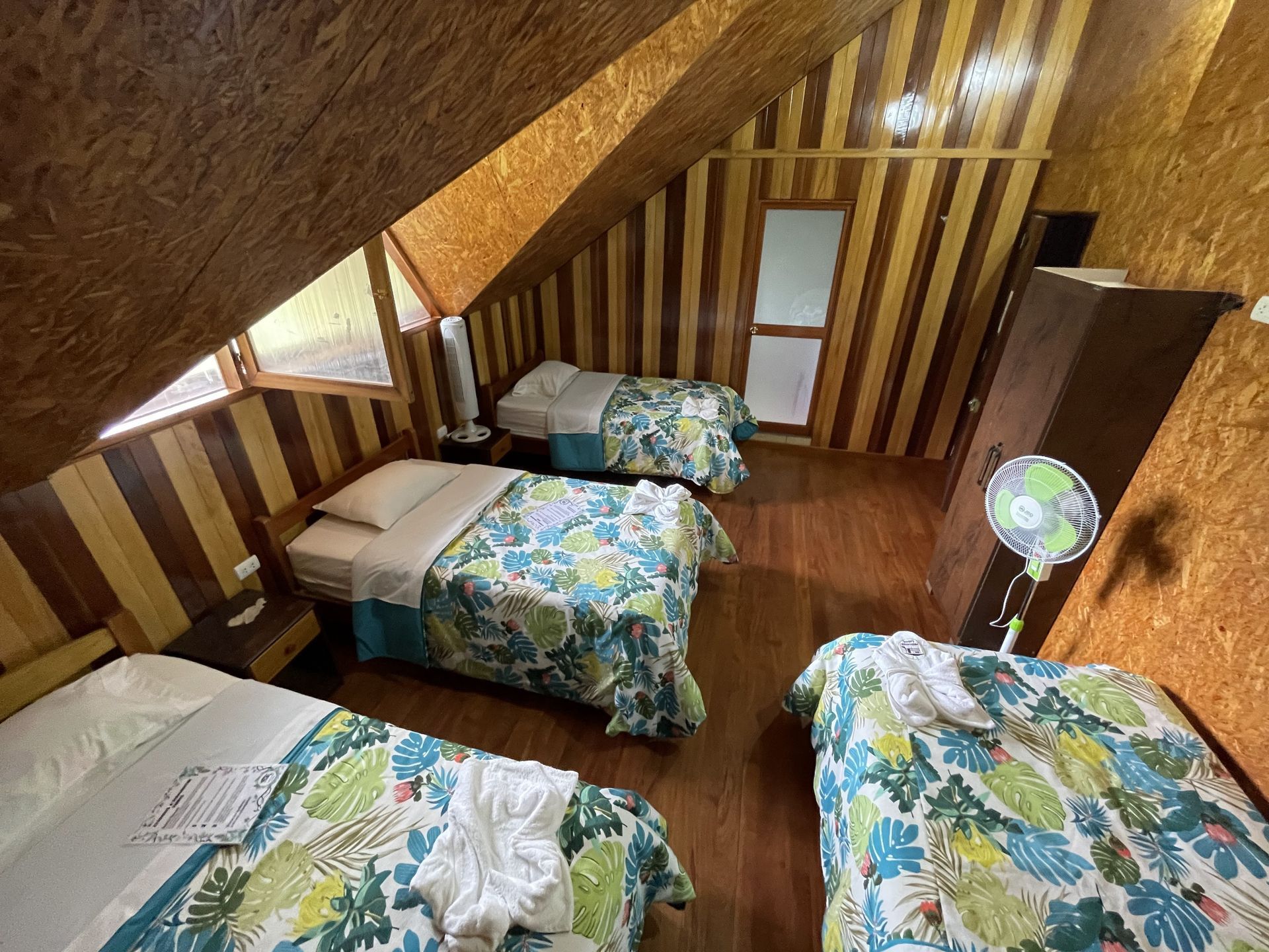 Un dormitorio con paredes de madera y techos inclinados, que cuenta con tres camas con ropa de cama de estampado.
