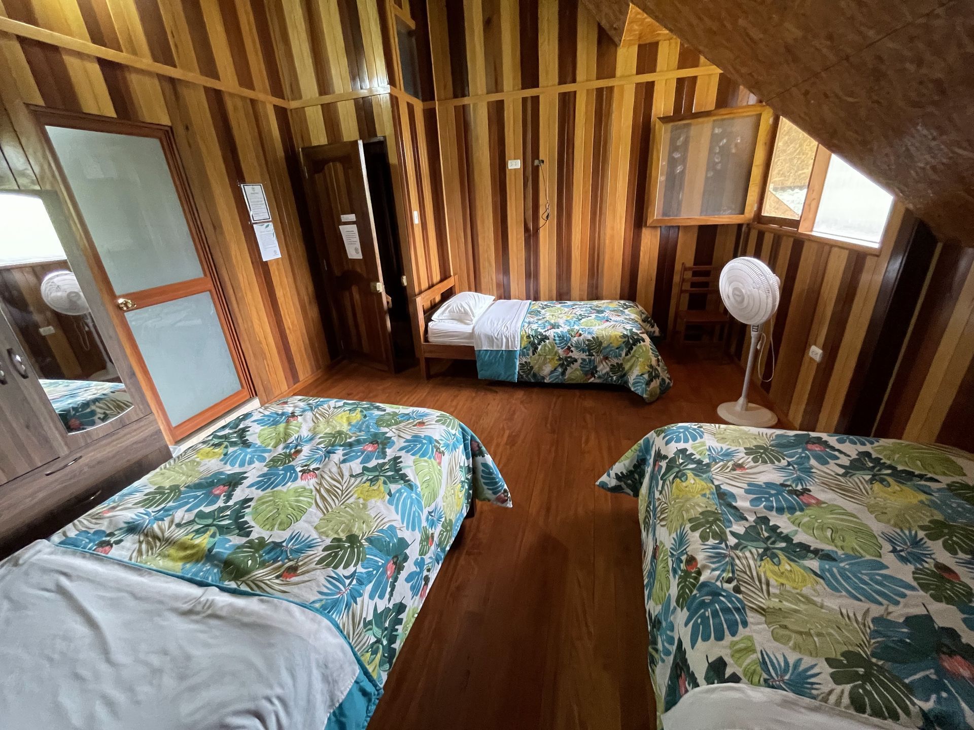 Un dormitorio con paredes revestidas de madera cuenta con tres camas con coloridas colchas de estampado tropical.