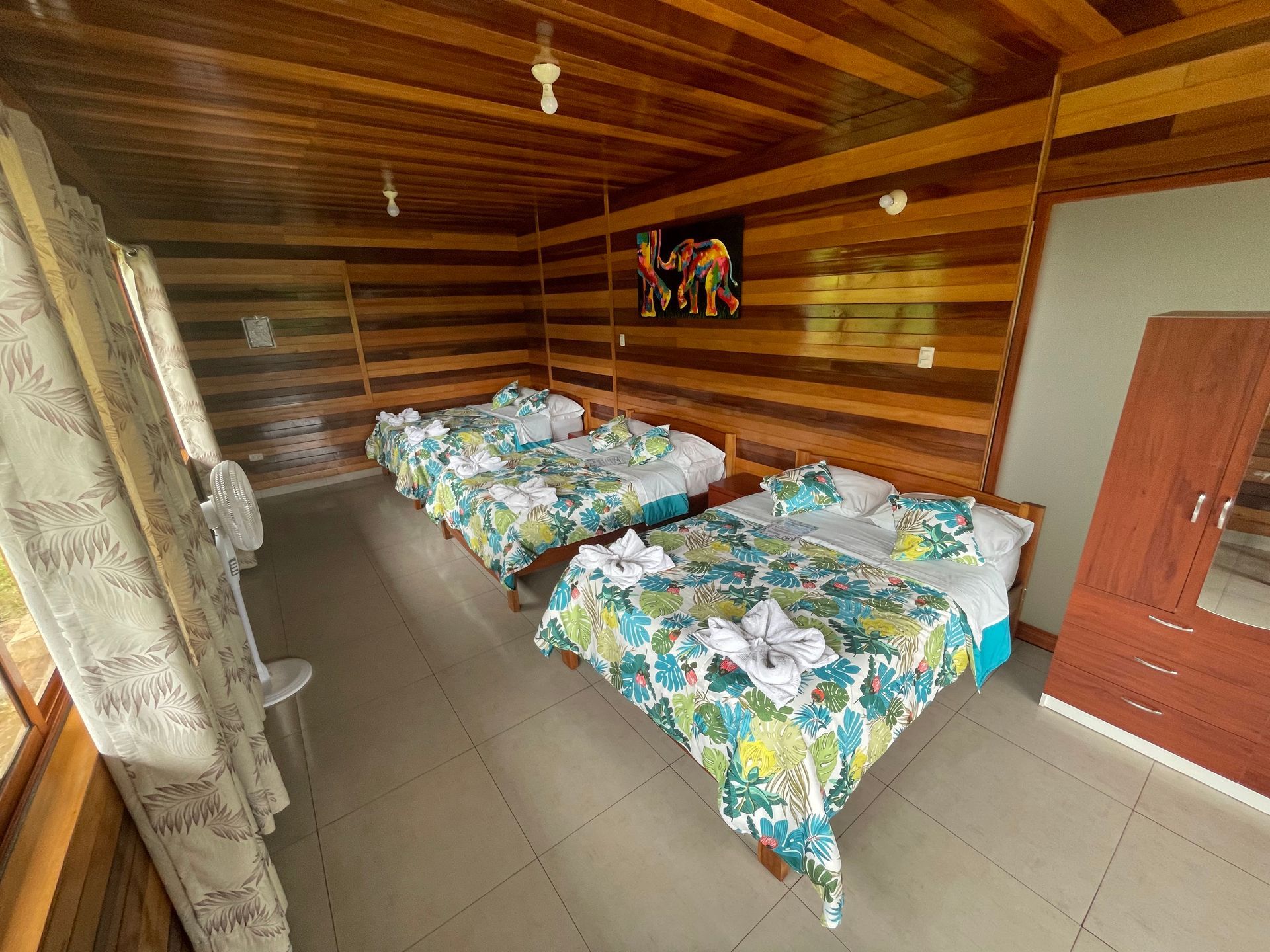 Un dormitorio rústico con paredes revestidas de madera, suelo de baldosas y dos camas con ropa de cama de color verde .