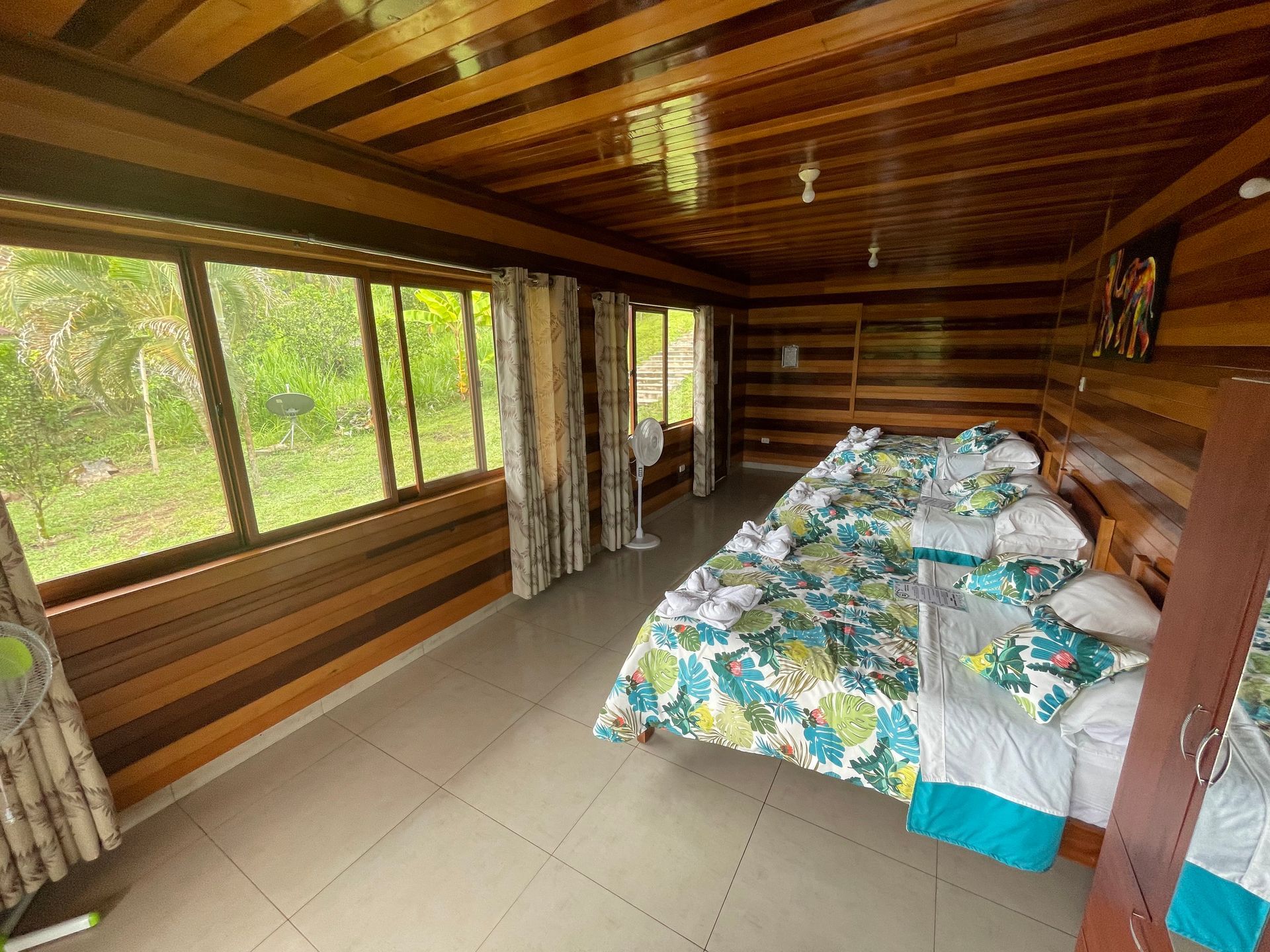 Un dormitorio rústico de madera con una fila de tres camas con ropa de cama estampada en blanco y verde azulado.