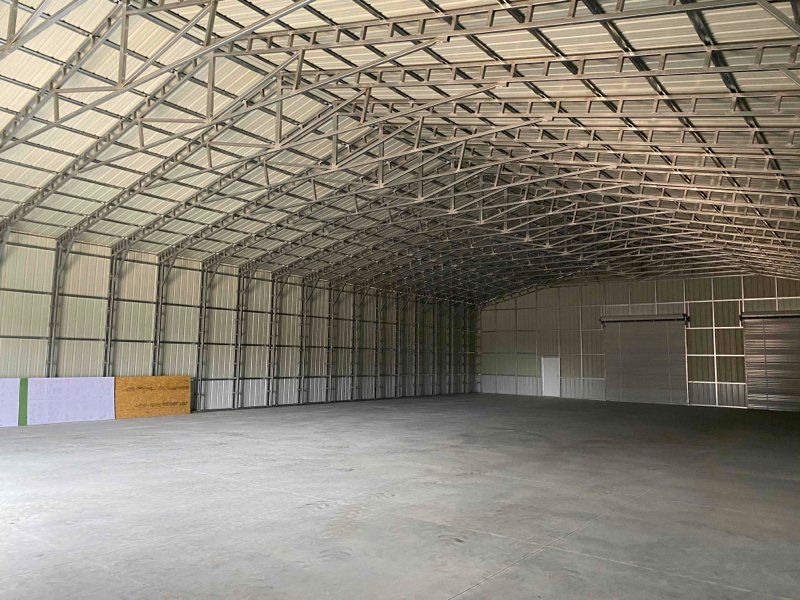 Empty metal-framed warehouse with arched ceiling and concrete floor; interior view.