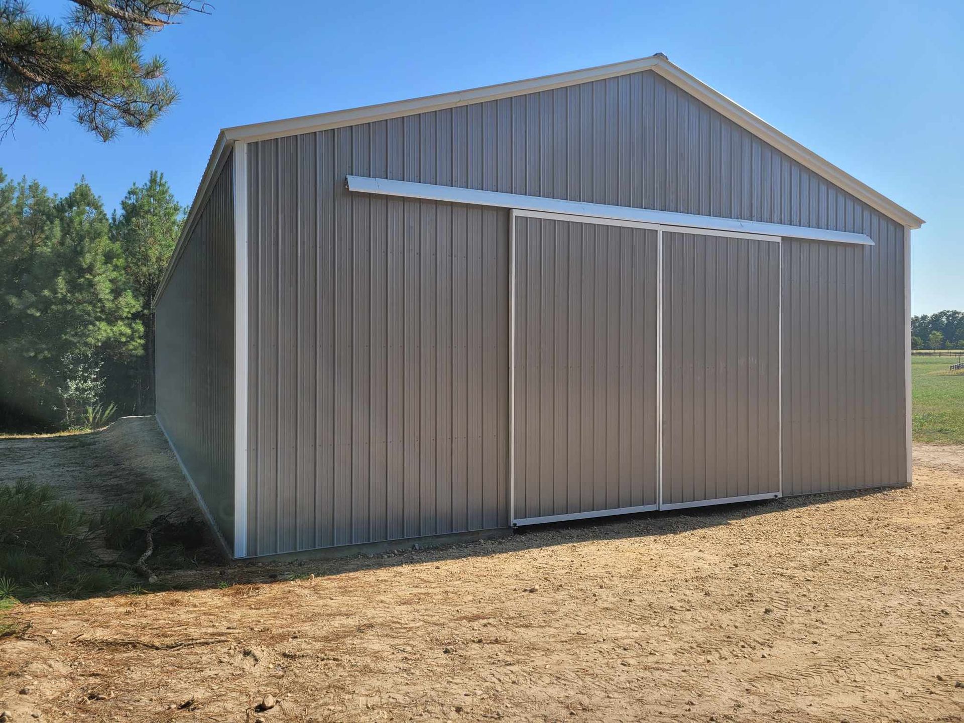 Gray metal shed with sliding door on a gravel lot. Trees in the background.