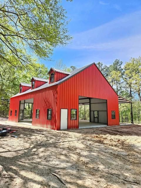 Red barn with large open bays, set against a backdrop of trees under a blue sky.