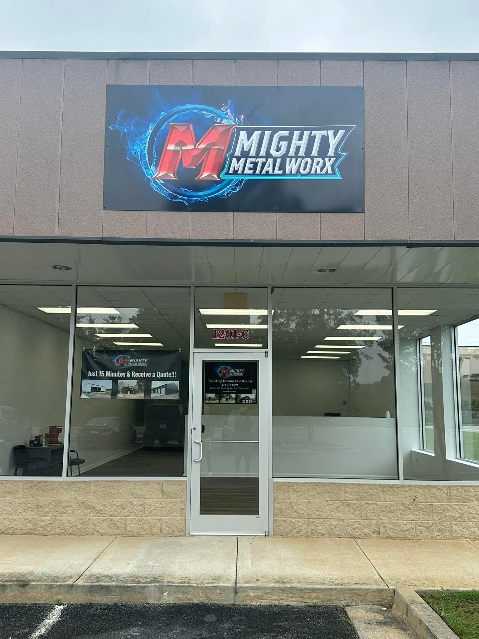 Exterior of Mighty Metal Worx shop; sign with logo above glass door and windows.